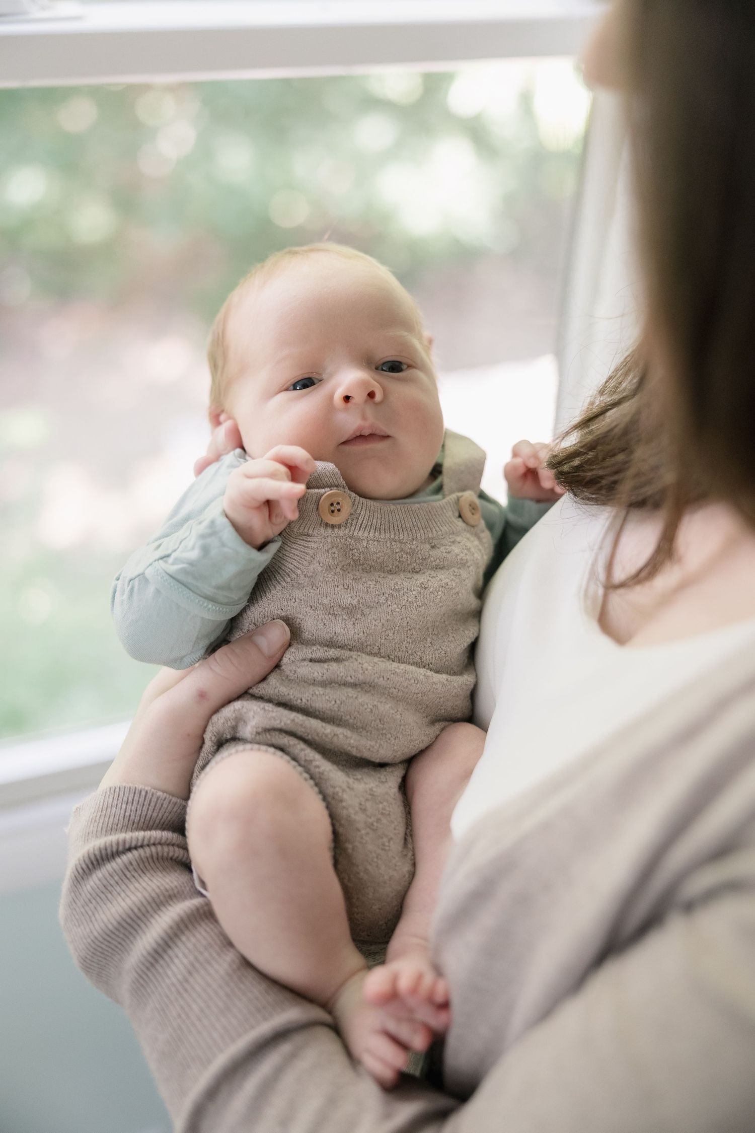 A baby in a gray knit romper rests peacefully in someone's arms during a tender moment.