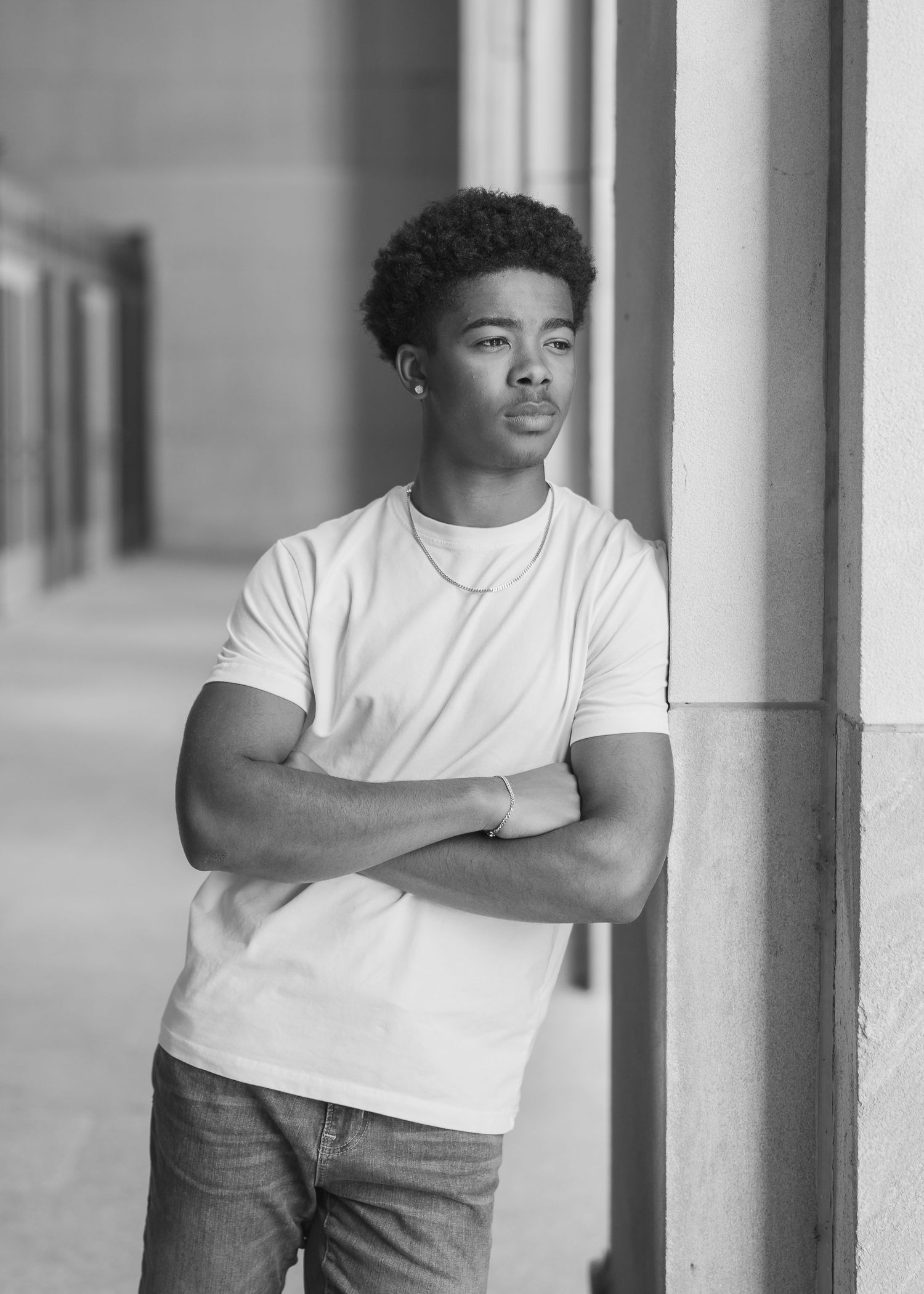 Person in white t-shirt and jeans stands with arms crossed in front of a light-colored wall.