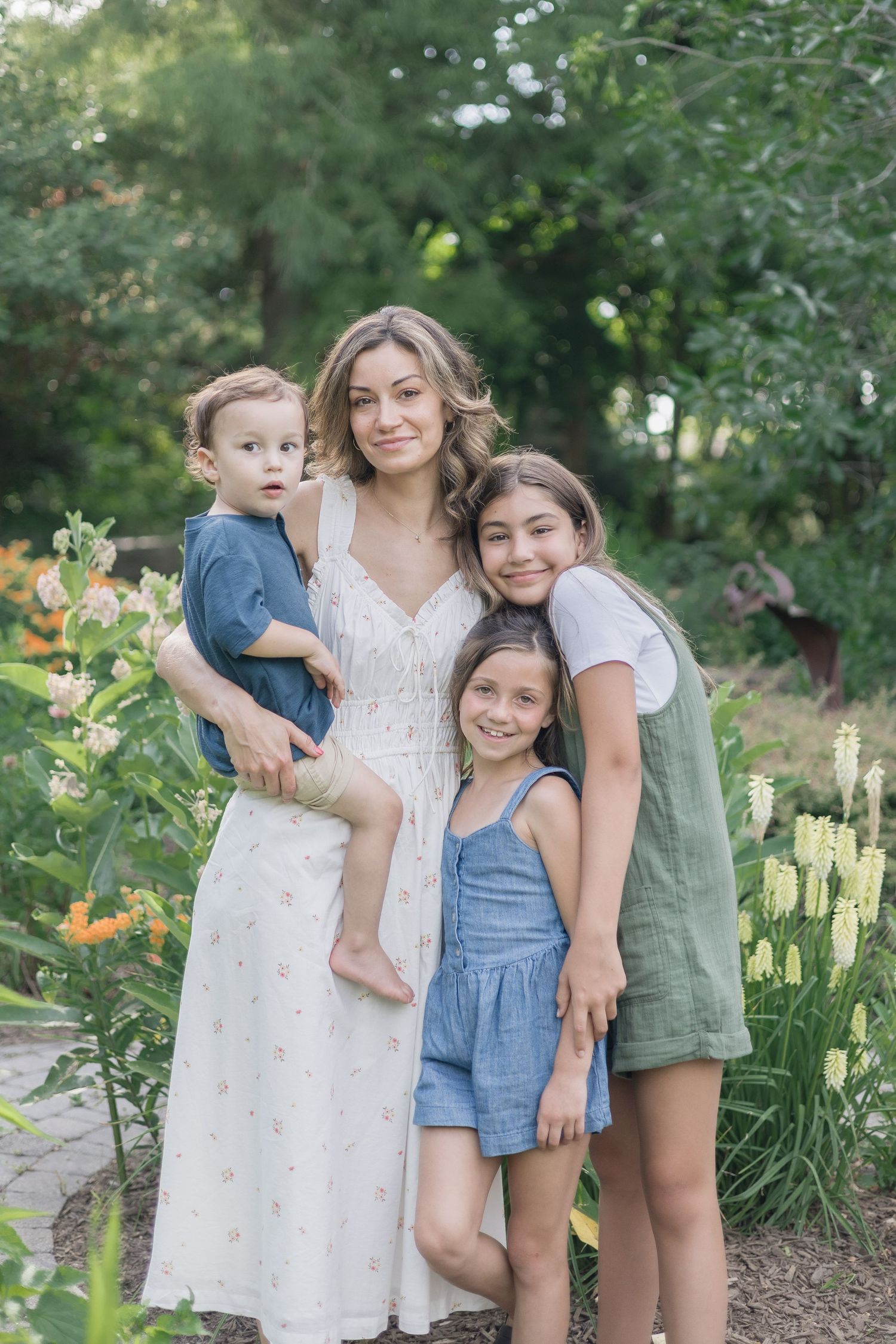 Family group poses together in a lush garden setting with blooming flowers on a summer day.