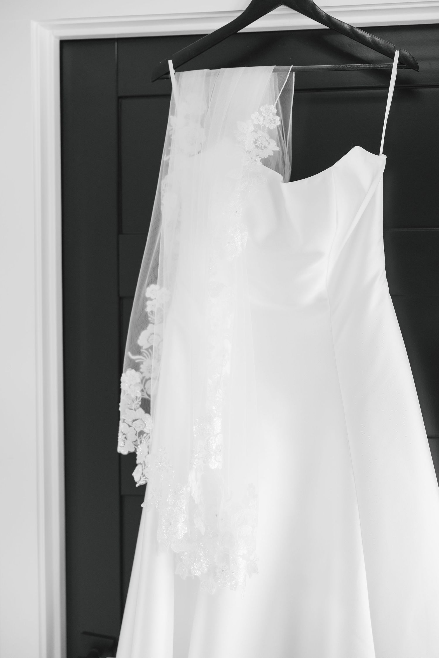 Black and white photo of an elegant strapless wedding dress with lace veil hanging on a hanger.