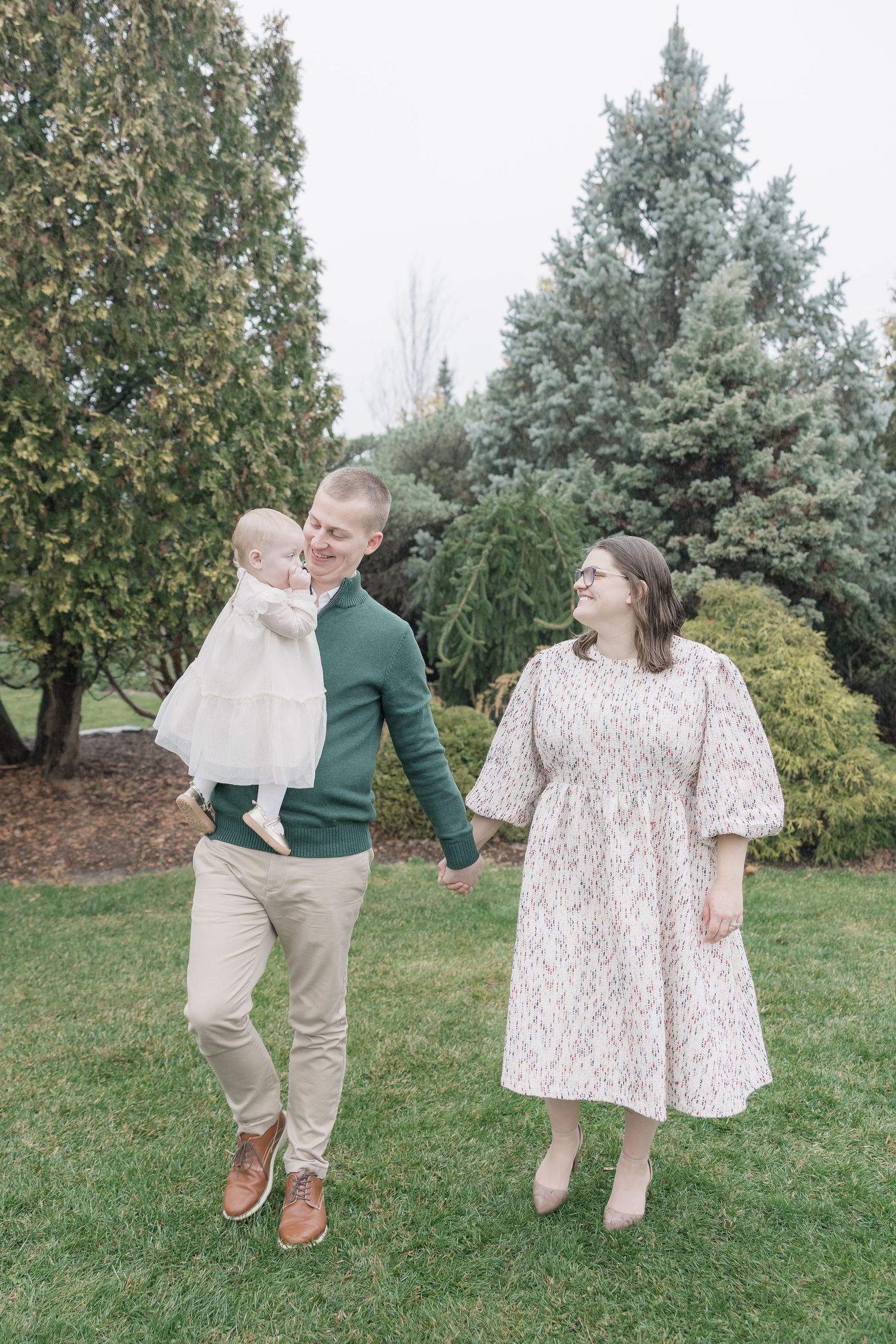 A family enjoying a playful moment together on a lawn with evergreen trees in the background.