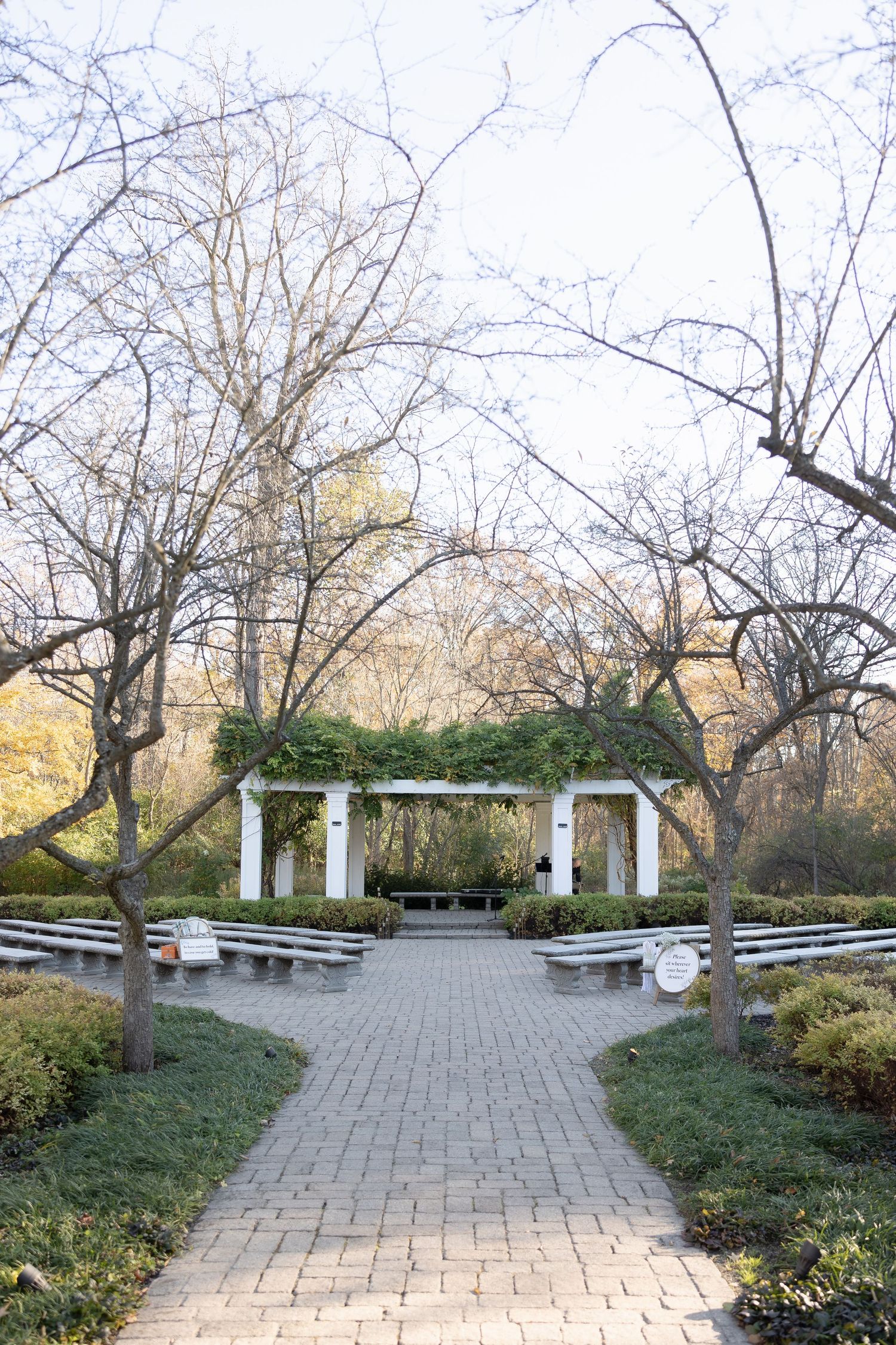 Stone pathway leading to a white columned wedding pergola surrounded by bare winter trees.