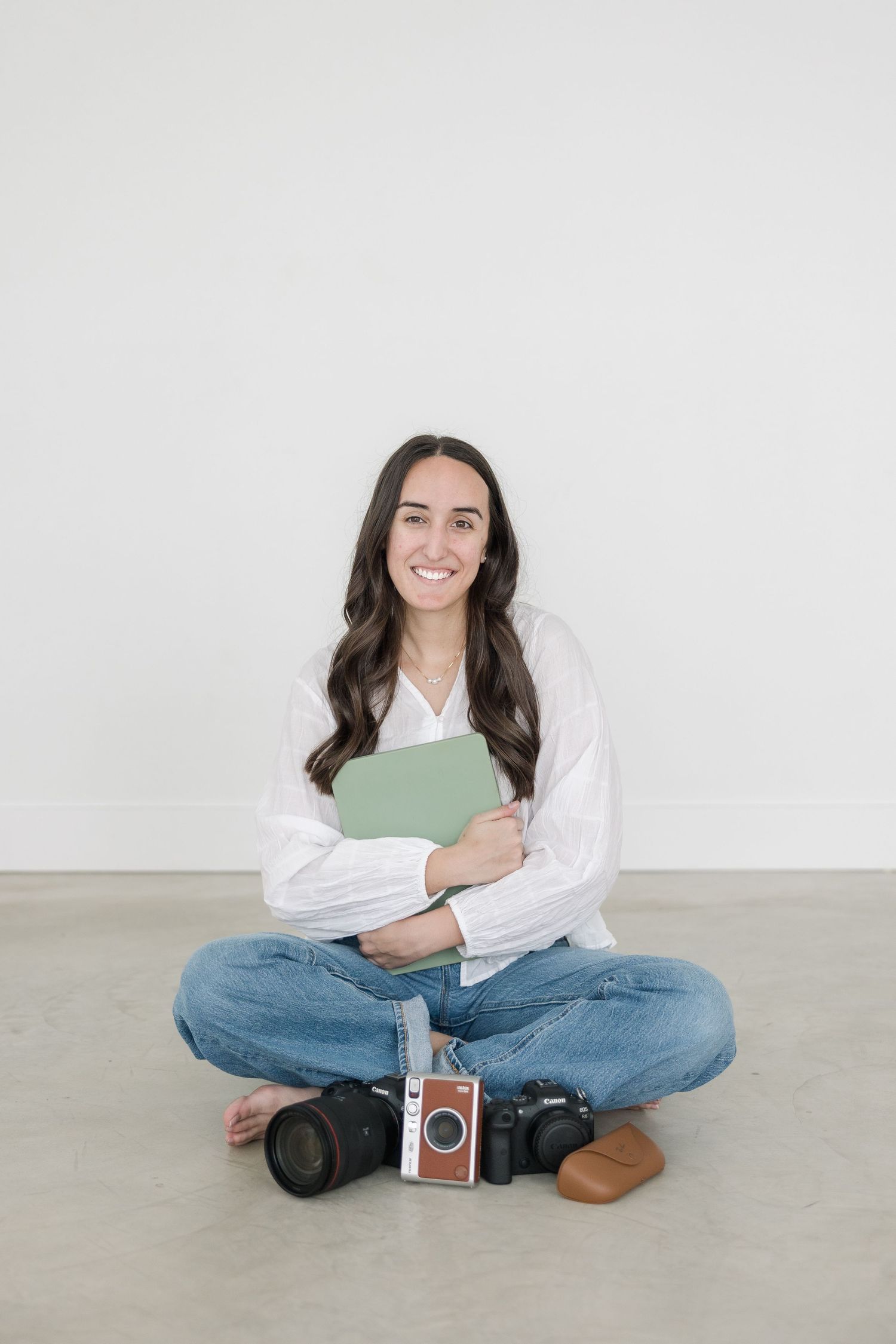 Person in casual attire sitting cross-legged on floor against white wall in multiple poses with vintage camera.