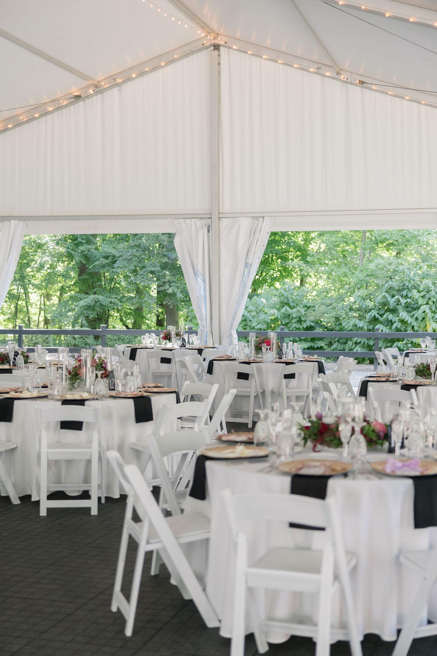 White wedding reception tent with round tables, folding chairs, and string lights creating an elegant outdoor venue setup.