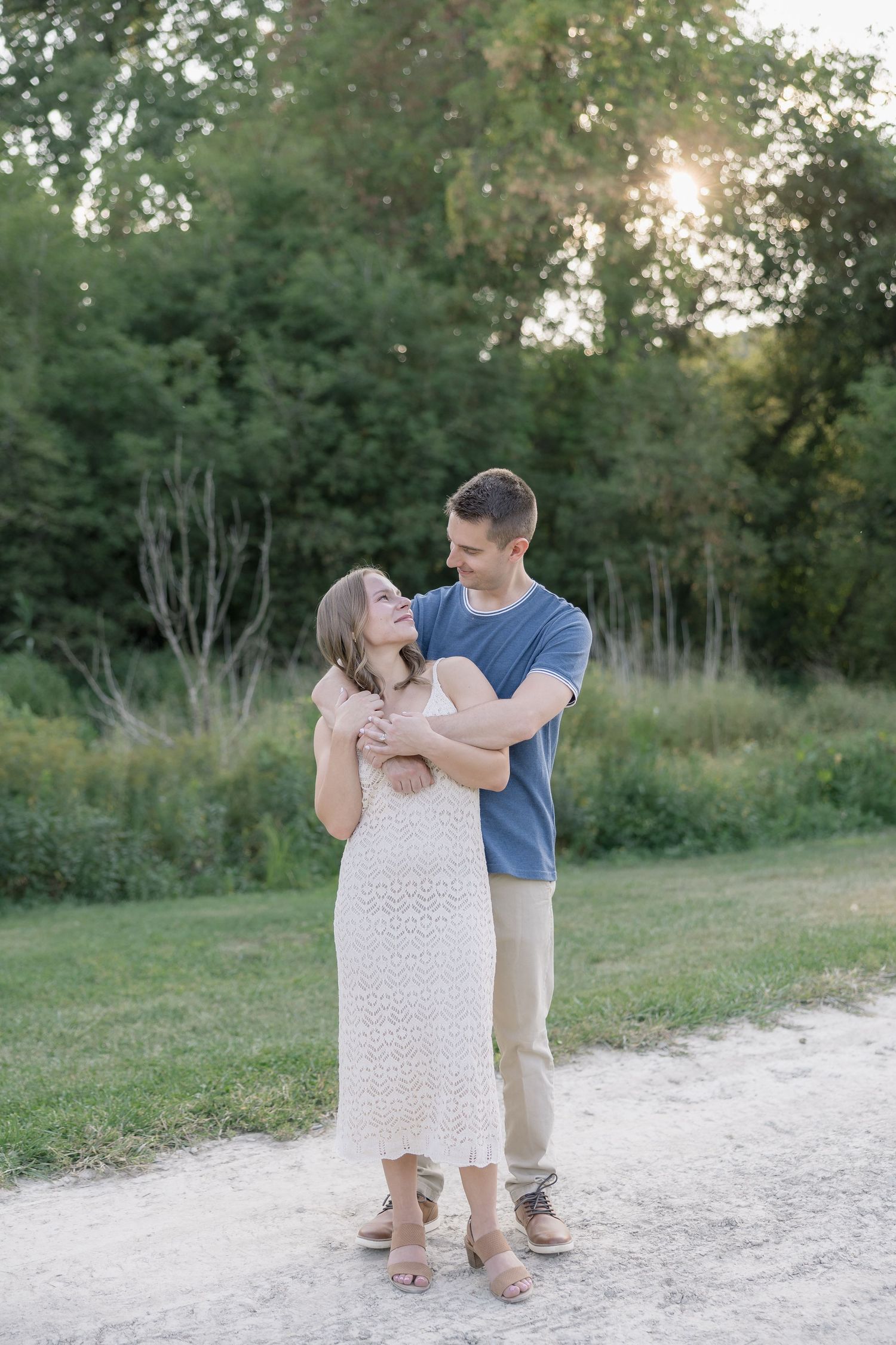 A couple shares a tender moment together on a dirt path surrounded by lush greenery at sunset.
