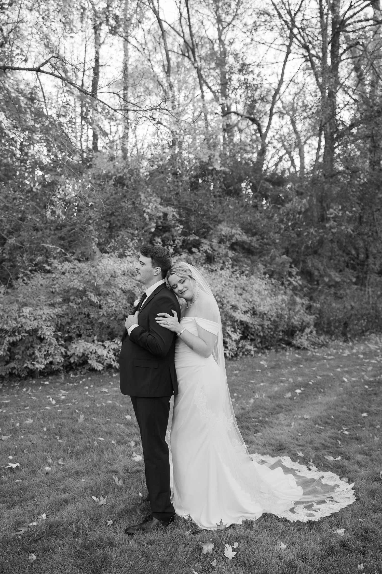 Black and white photo of wedding couple embracing in a wooded outdoor setting.