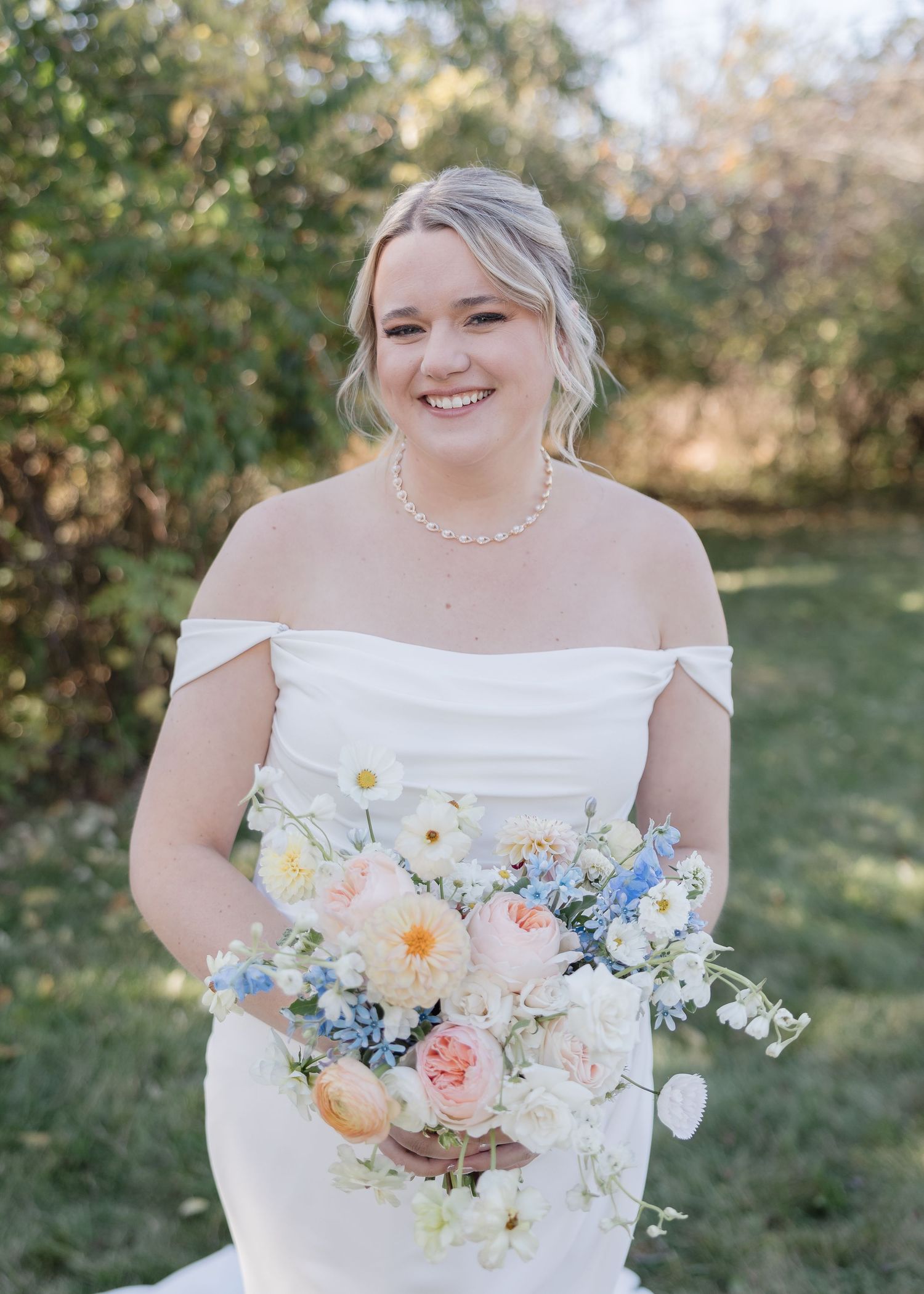 A beautiful springtime bridal portrait showing off an off-the-shoulder white gown and pastel bouquet with pearls.