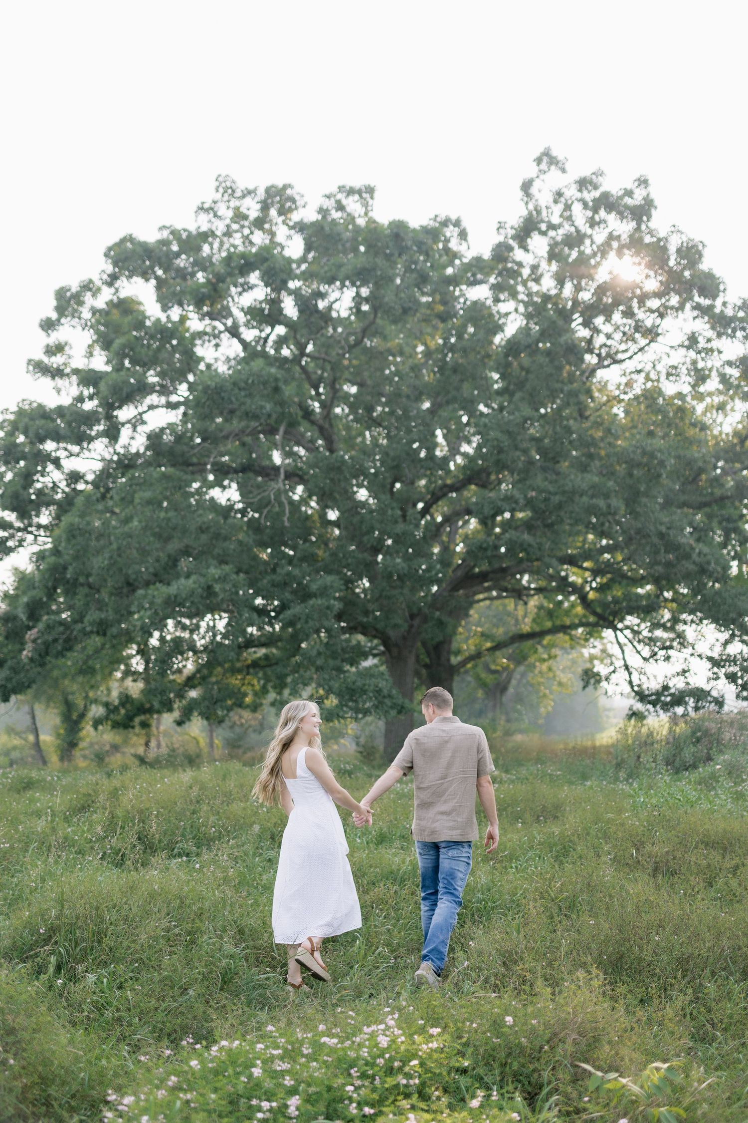 A couple holding hands while walking through a wildflower meadow on a sunny summer afternoon.