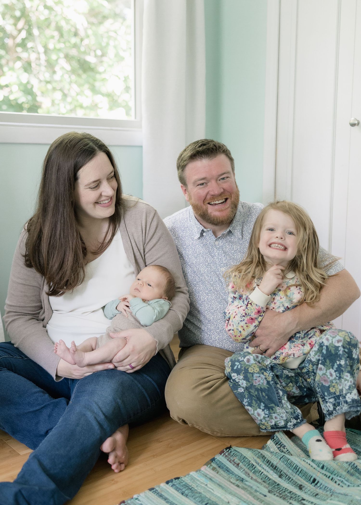 A family shares playful candid moments together while sitting on a hardwood floor in their bright home.