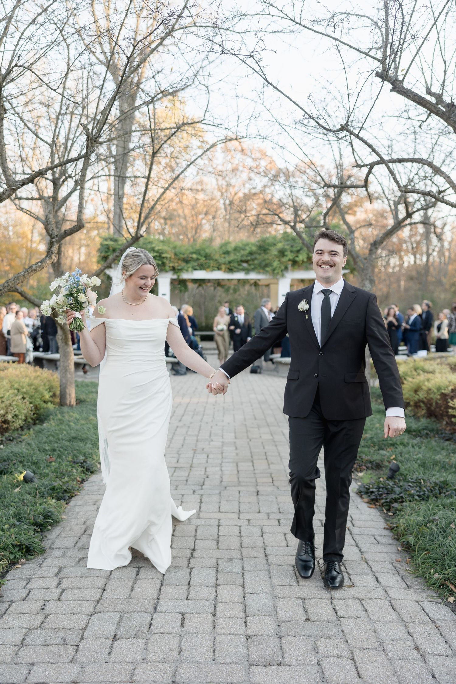 A joyful wedding couple walking hand in hand down a stone pathway.