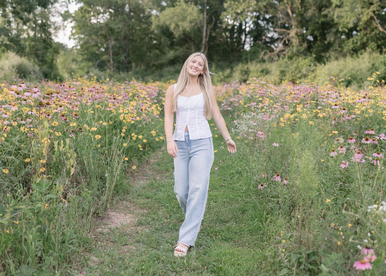 A person walks through a vibrant wildflower meadow filled with pink cosmos flowers on a sunny summer day.