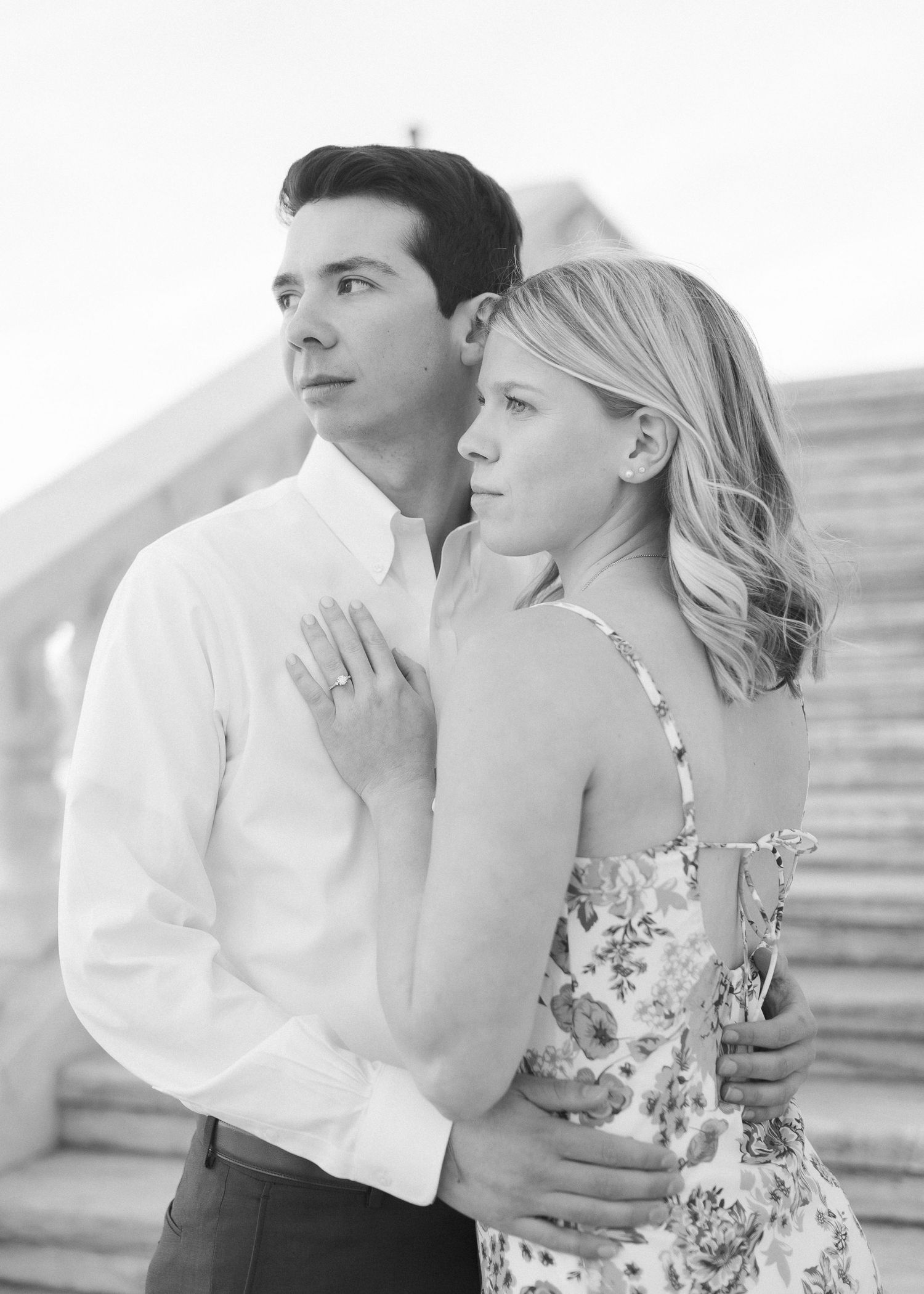 Black and white portrait of a couple in formal attire embracing while looking into the distance.