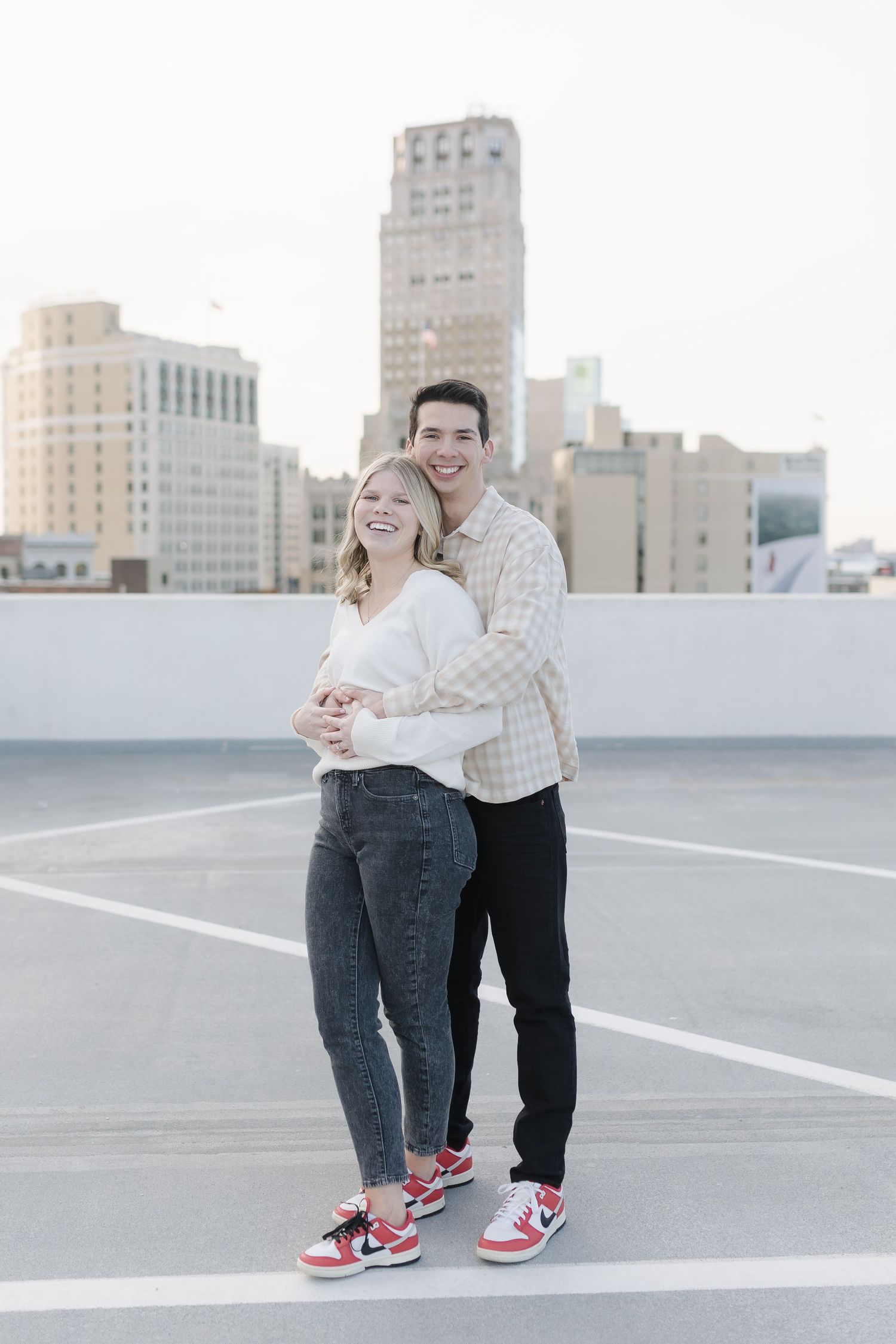 Happy couple embracing and laughing together on a rooftop with urban skyline backdrop.