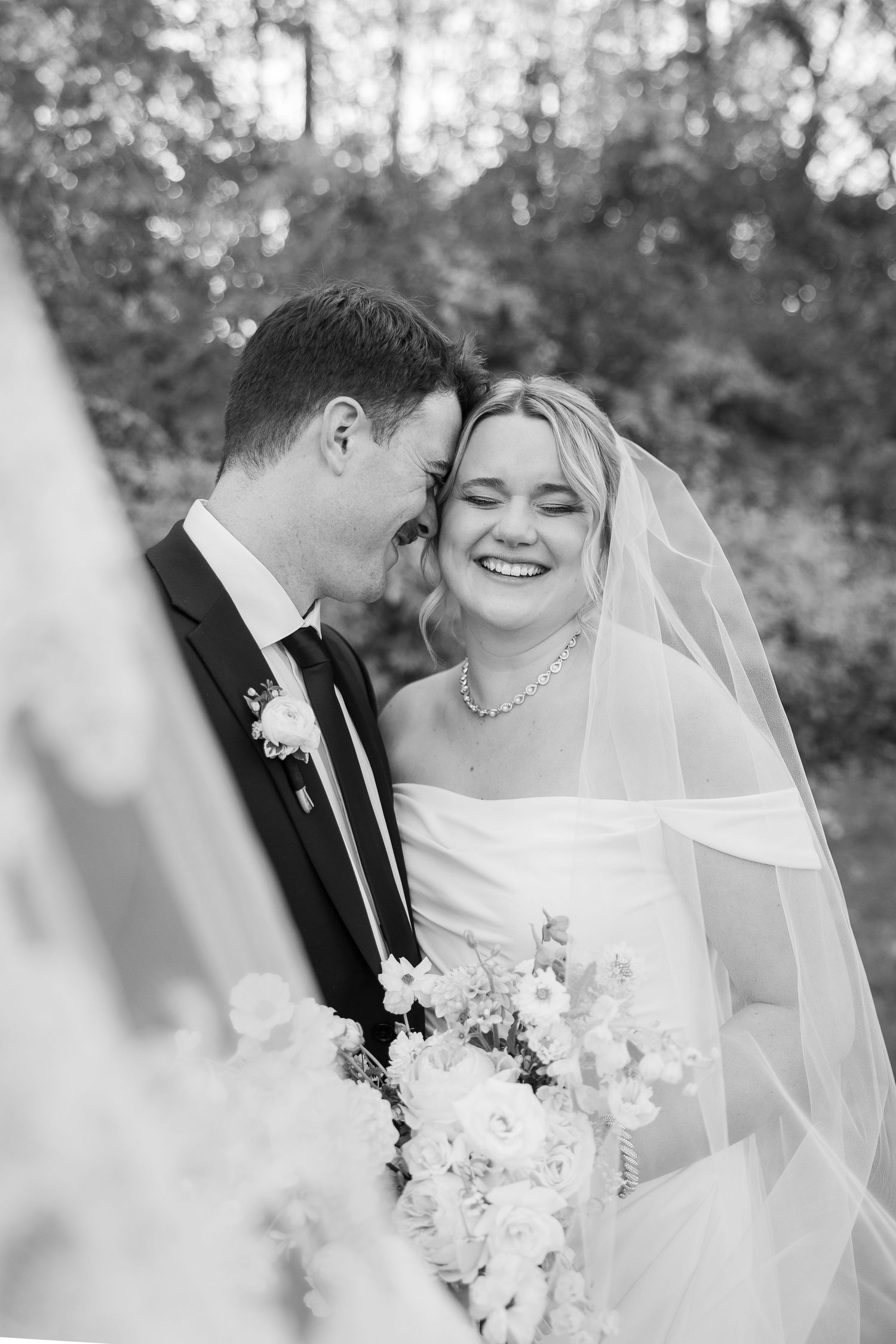 Black and white portrait of newlyweds sharing a joyful moment with bride holding white bouquet.