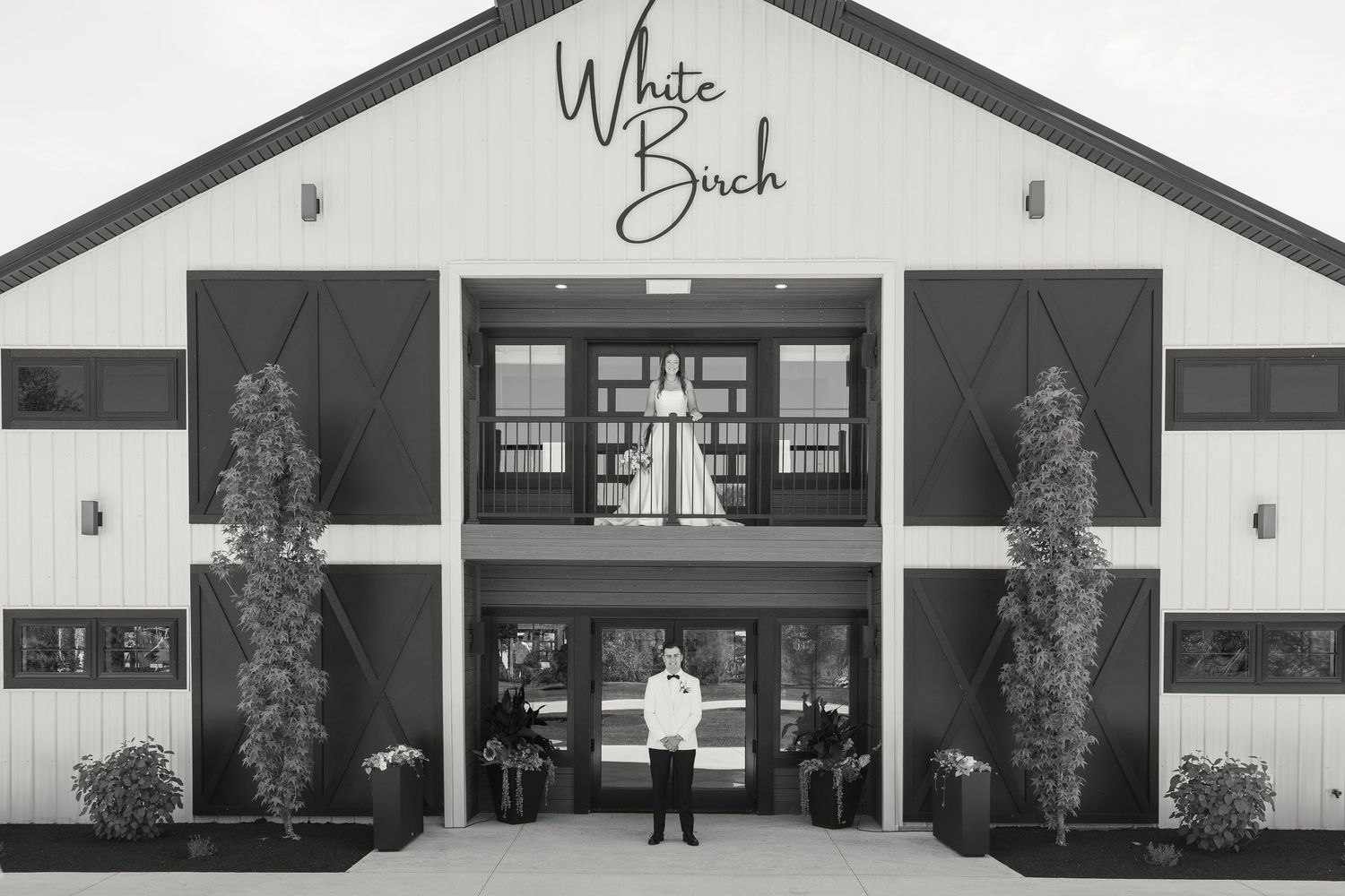 Black and white photo of a person standing at the entrance of White Birch venue with elegant barn doors.