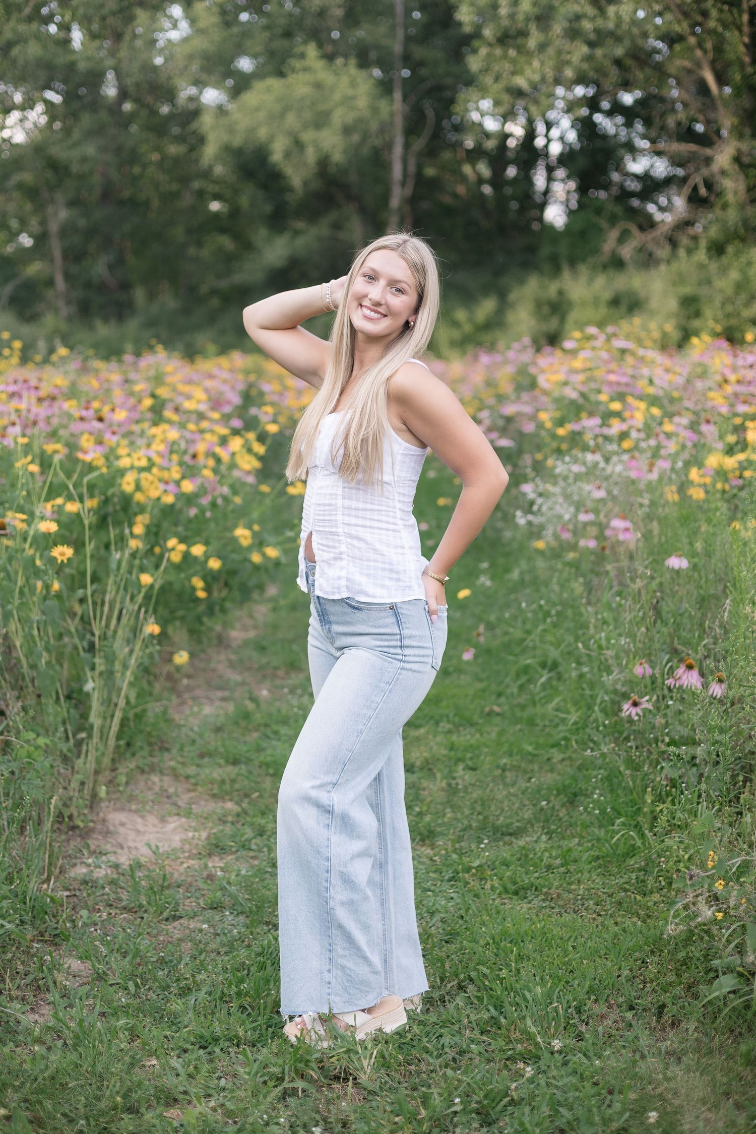 A person in a white summer dress poses playfully in a vibrant wildflower meadow on a sunny afternoon.