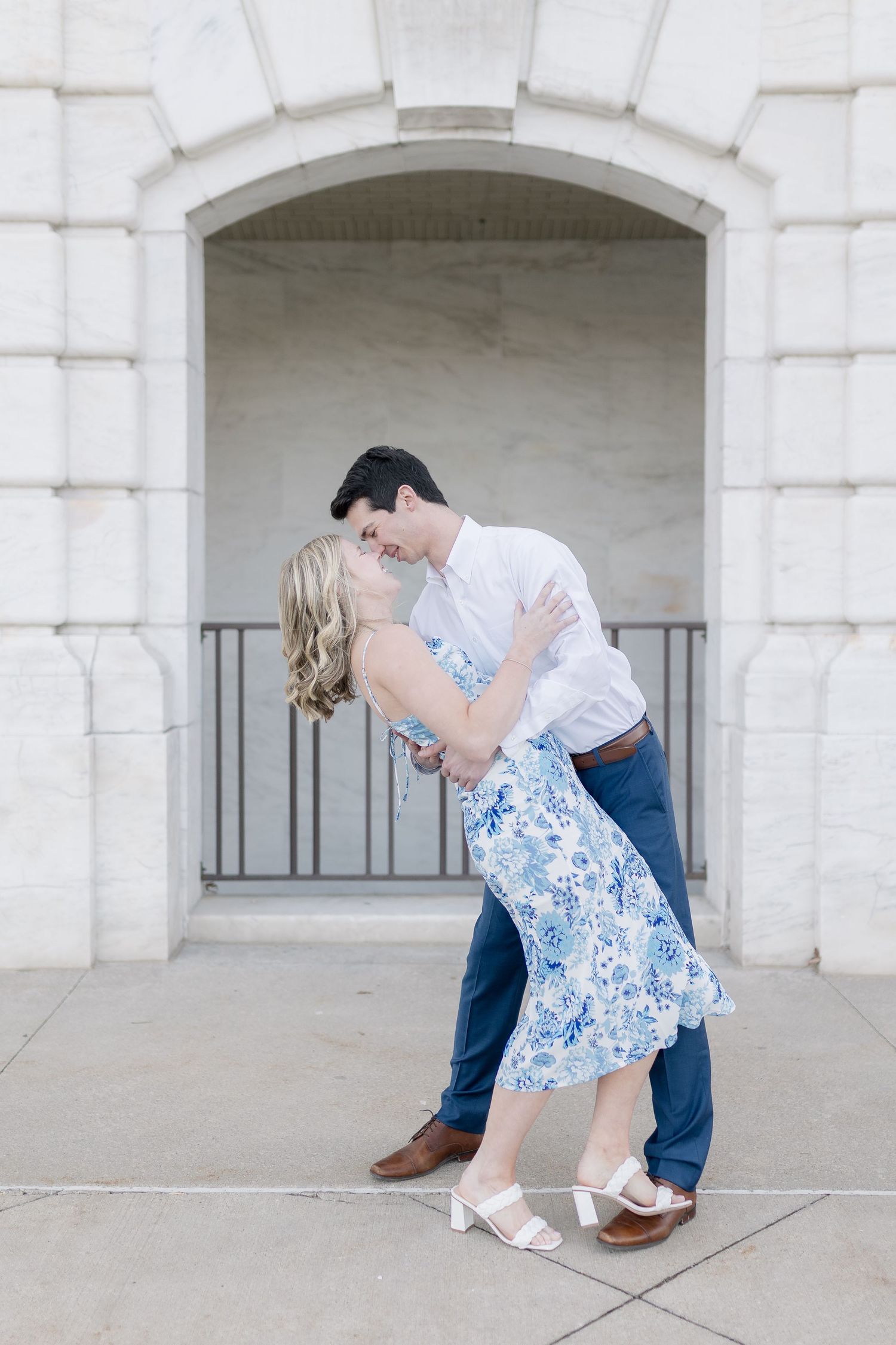 A romantic embrace under a white stone archway with classic architectural details.