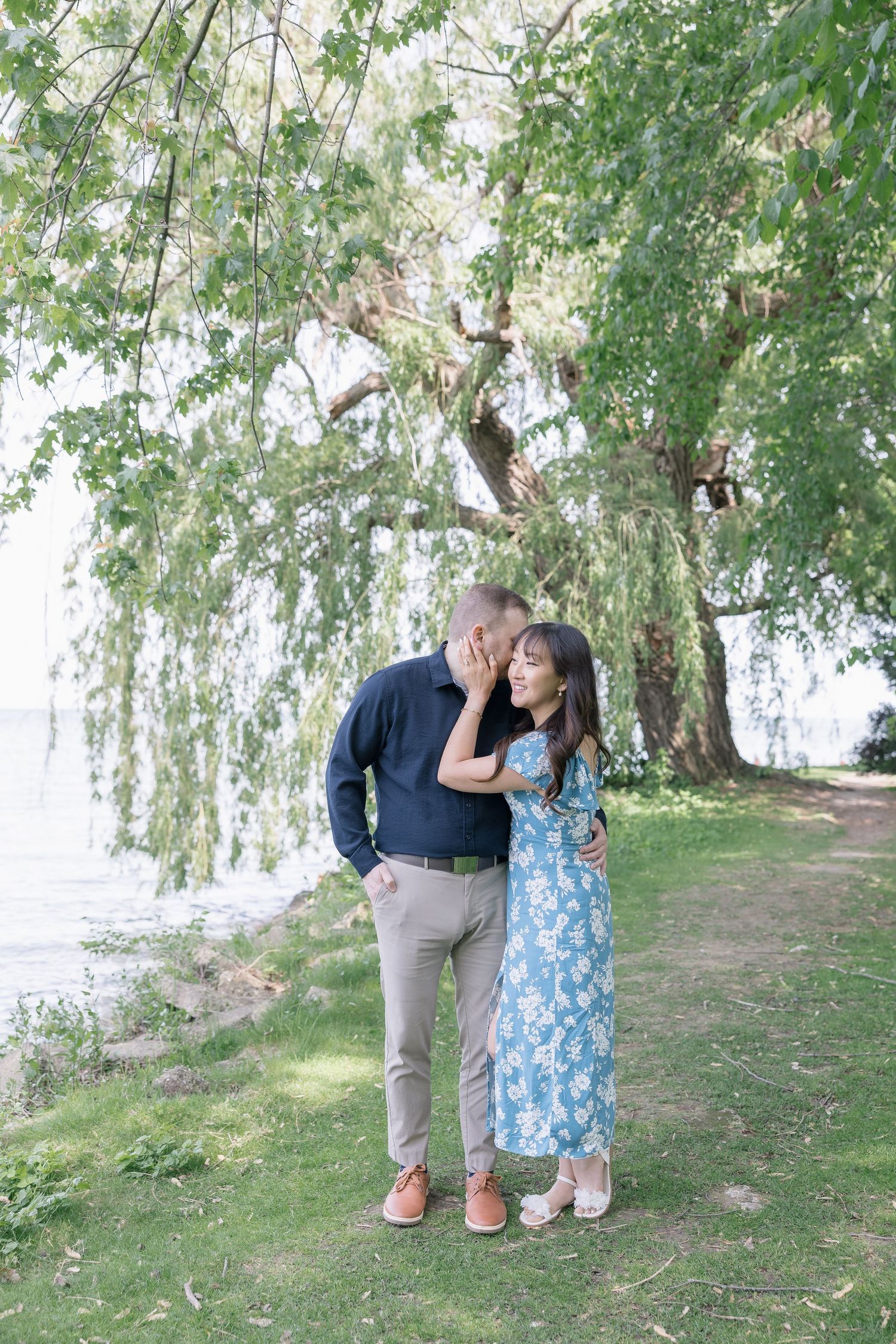 A sweet moment between two people under weeping willow trees by a lake.