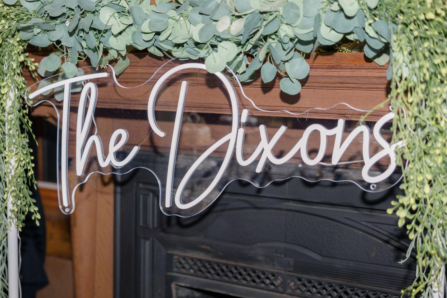 Neon sign reading 'The Dixons' mounted on wood panel with cascading greenery decoration.