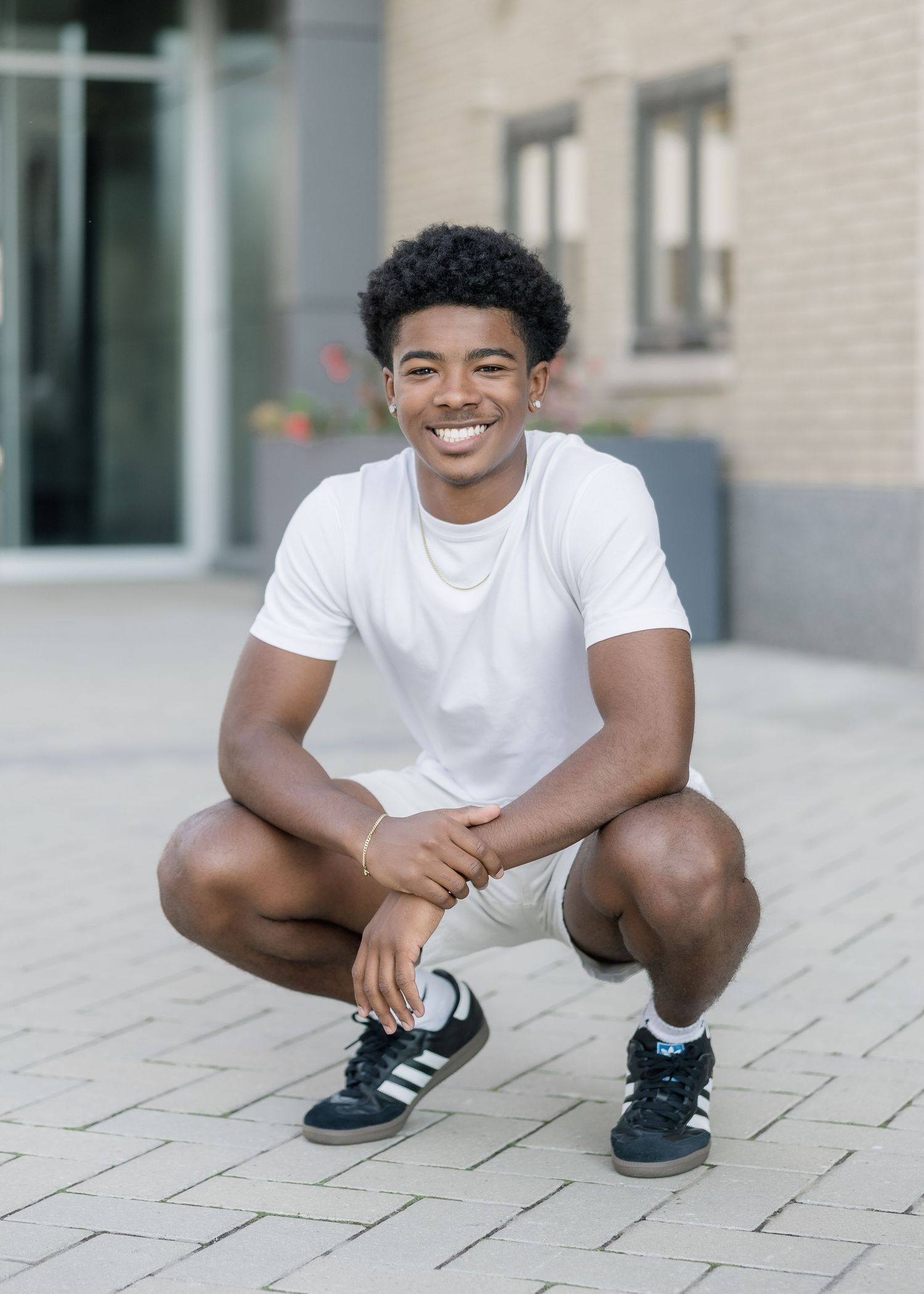 A person wearing a white t-shirt and black shorts crouches down on a paved stone walkway.