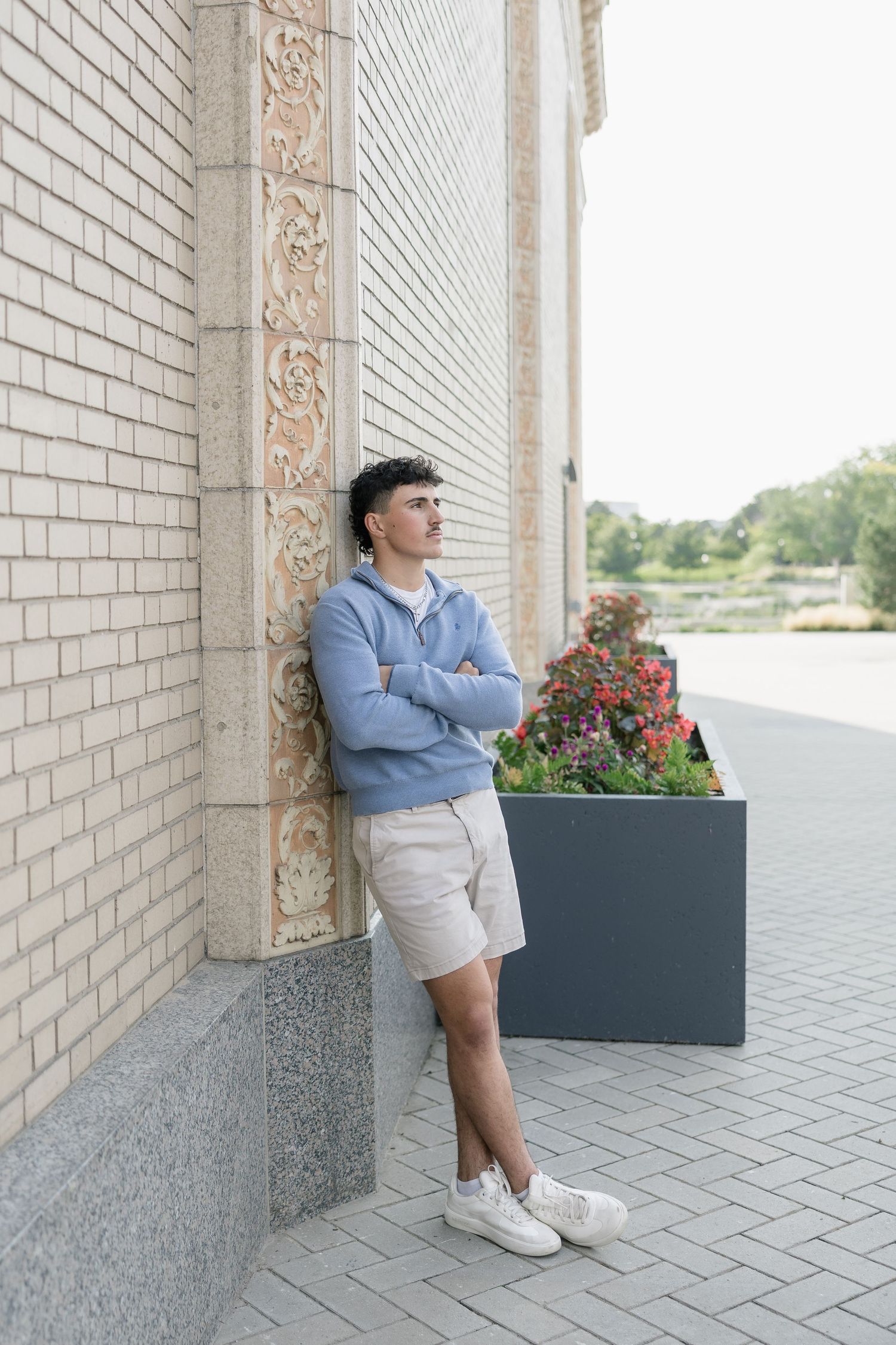 Person in light blue shirt and grey shorts leans against white brick wall near decorative planters.
