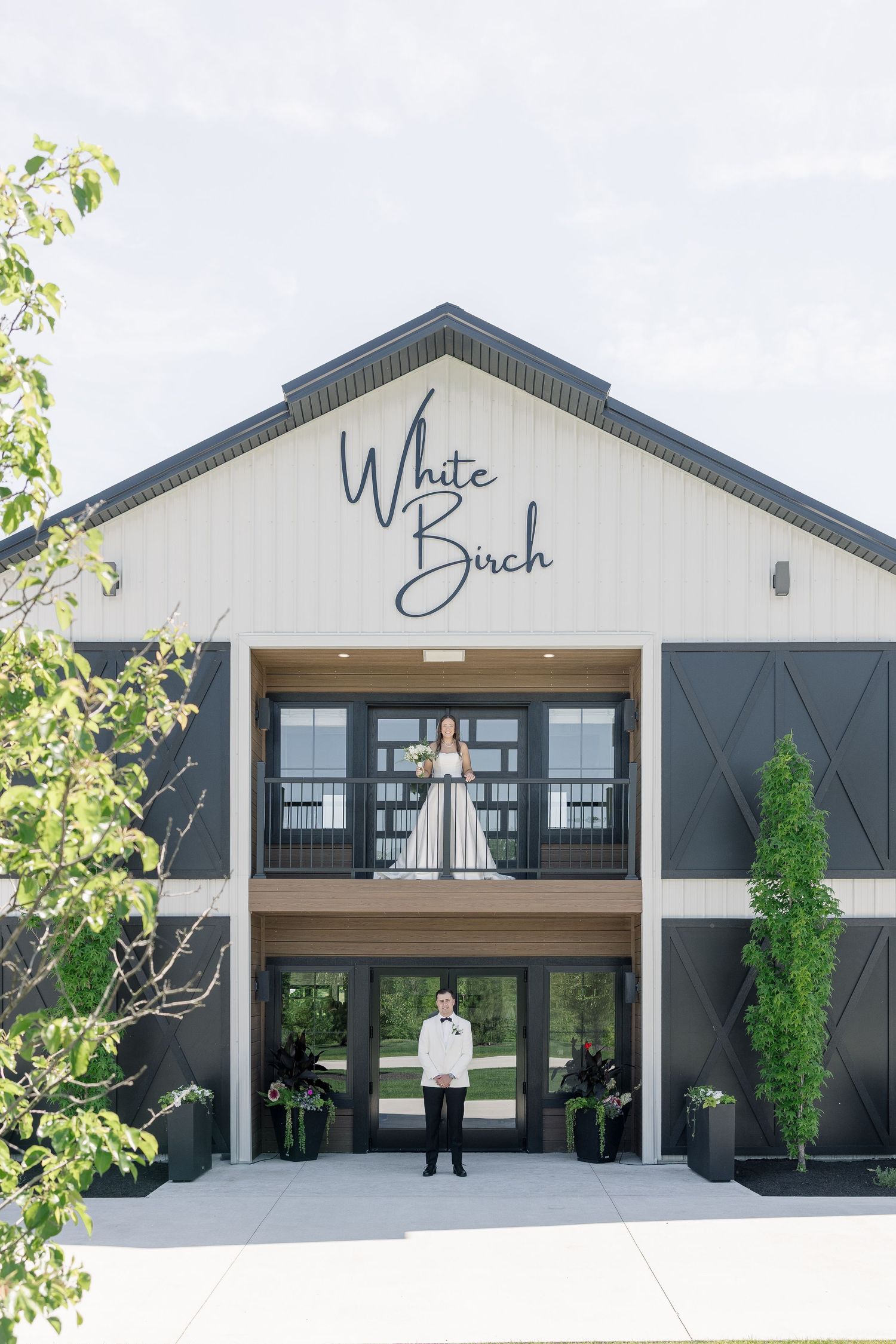 Bride and groom pose at White Birch wedding venue, one on balcony and one at entrance doors.
