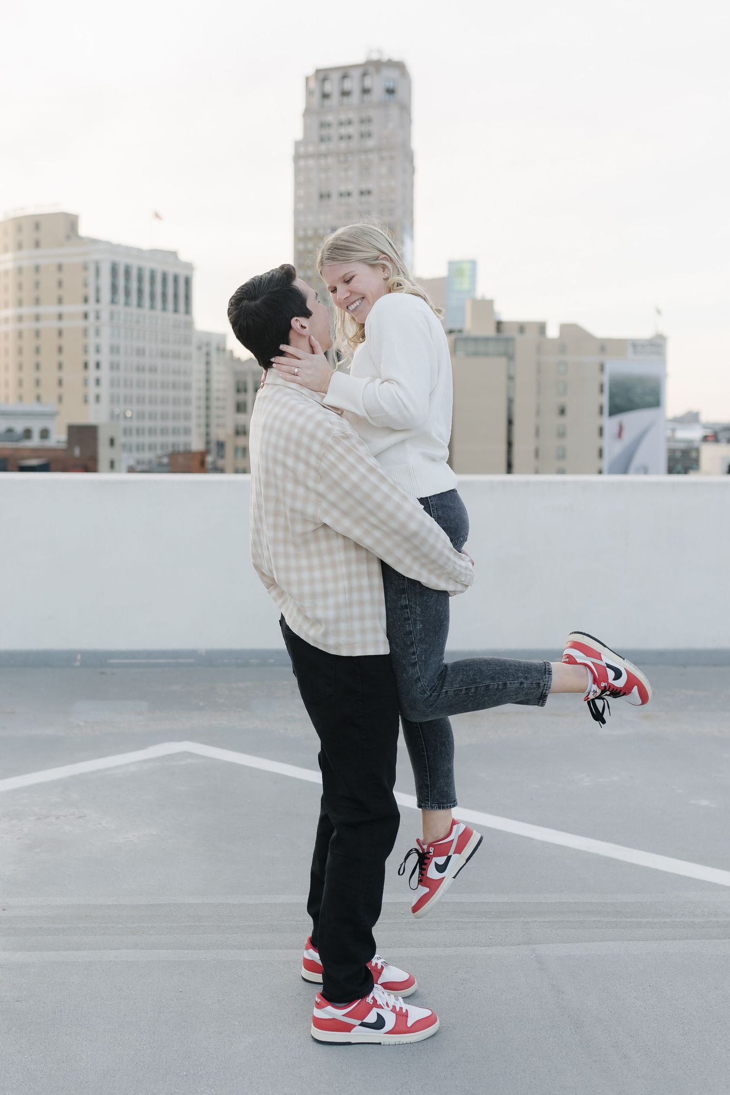 A romantic moment on a rooftop parking deck with an urban skyline backdrop.