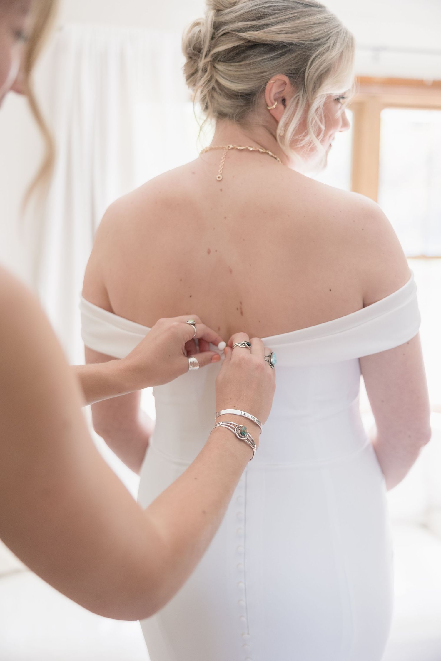 A wedding dress fitting showing detailed off-shoulder design and back closure.