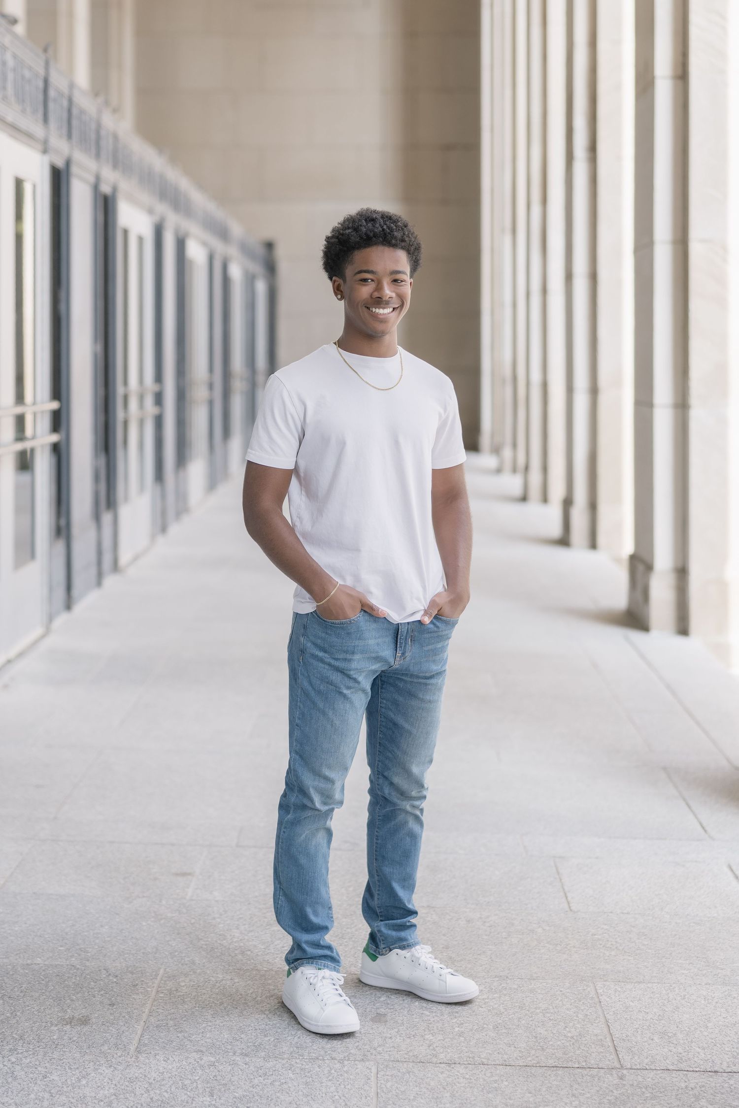 Person wearing casual white t-shirt and blue jeans walks down bright hallway with columns.