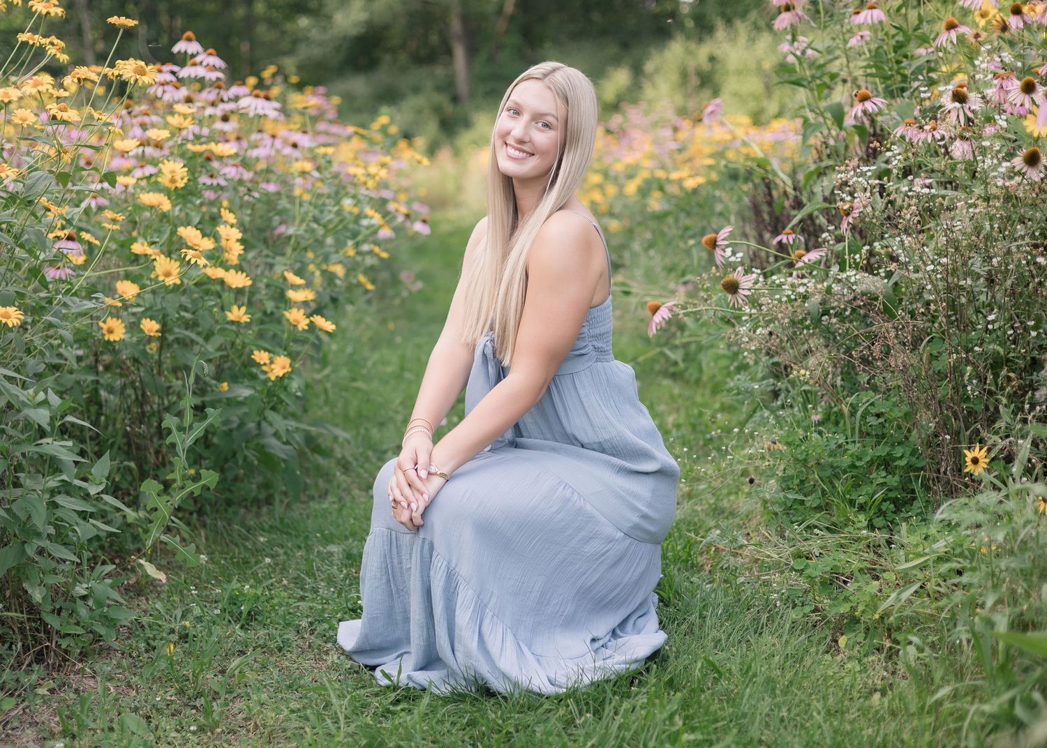 A person in a flowing blue dress sits gracefully among vibrant wildflowers in a summer garden.