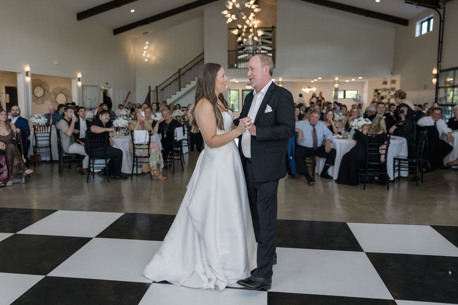 Bride and groom share their first dance on a black and white checkered floor at an elegant wedding reception.
