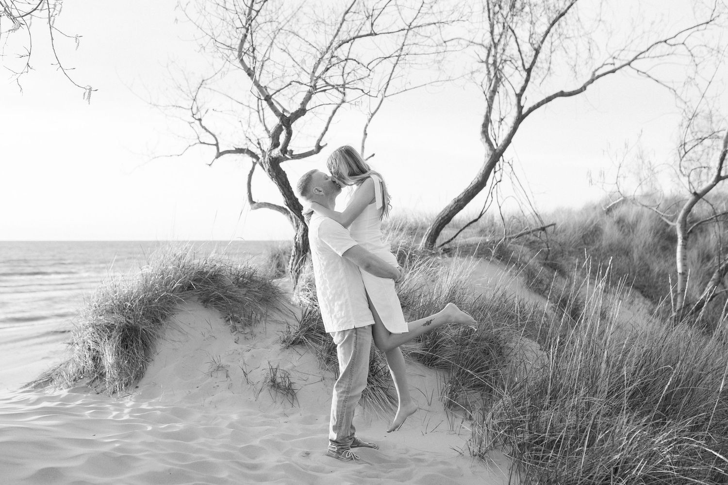People walking and playing along a misty beach with sand dunes and tall grass.