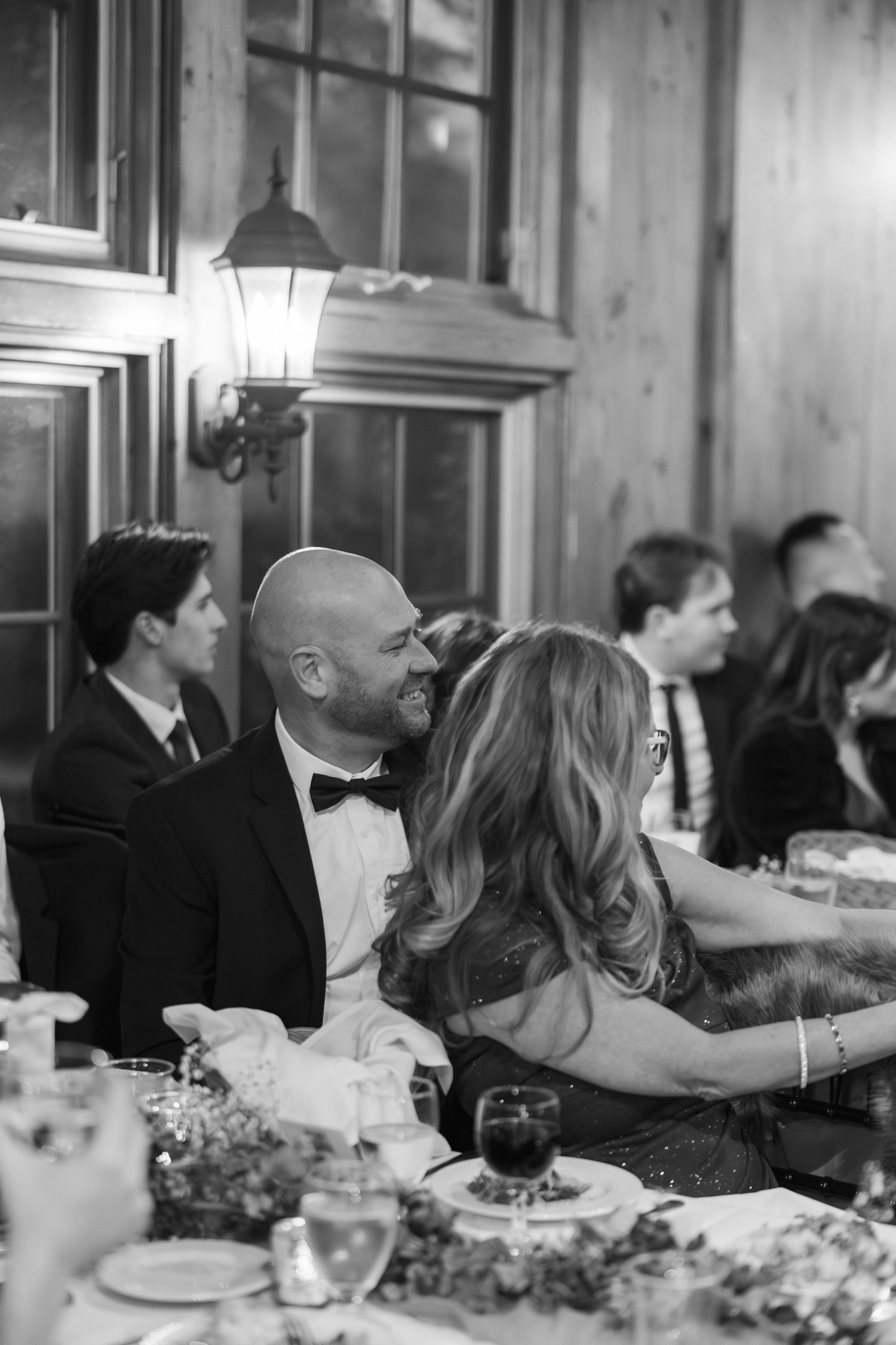 Black and white candid photo of wedding guests dining at elegant reception.