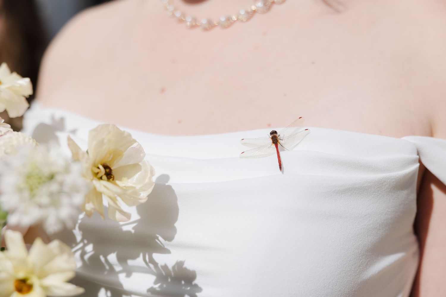 Close-up detail of a pearl necklace and white floral arrangement against a wedding dress.