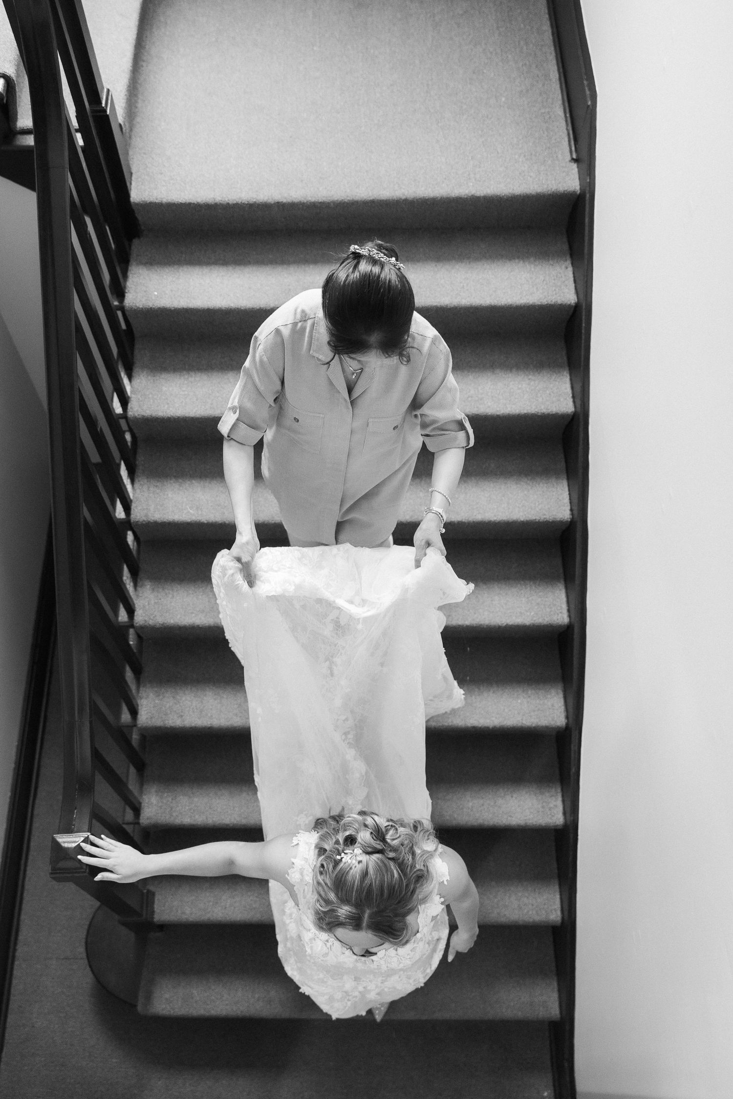 Black and white overhead view of someone sitting on stairs in a flowing white dress.