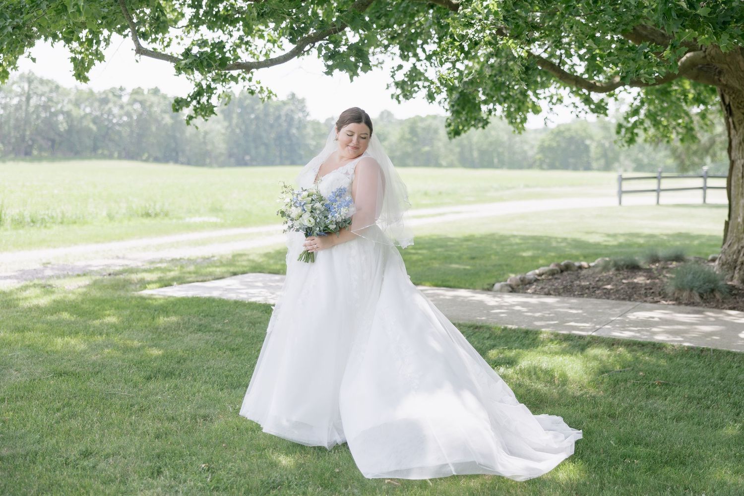 A flowing white wedding dress twirls gracefully in an outdoor garden setting with lush green trees in the background.