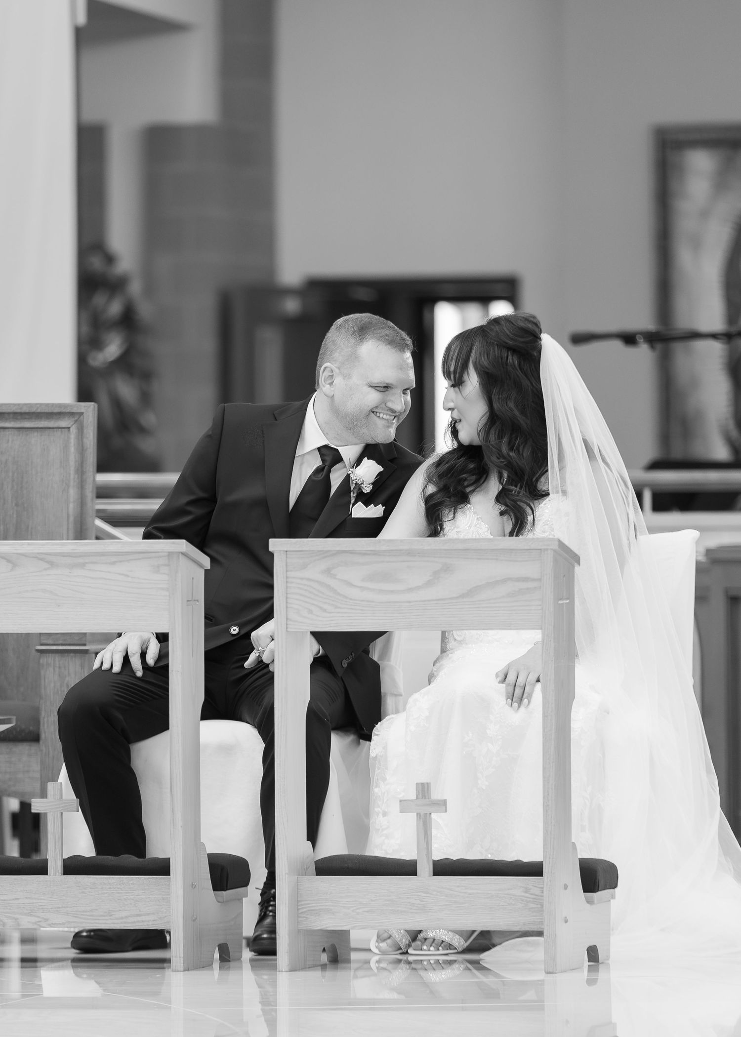 Black and white photo of a bride and groom sharing a tender moment while seated at the altar during their church wedding ceremony.