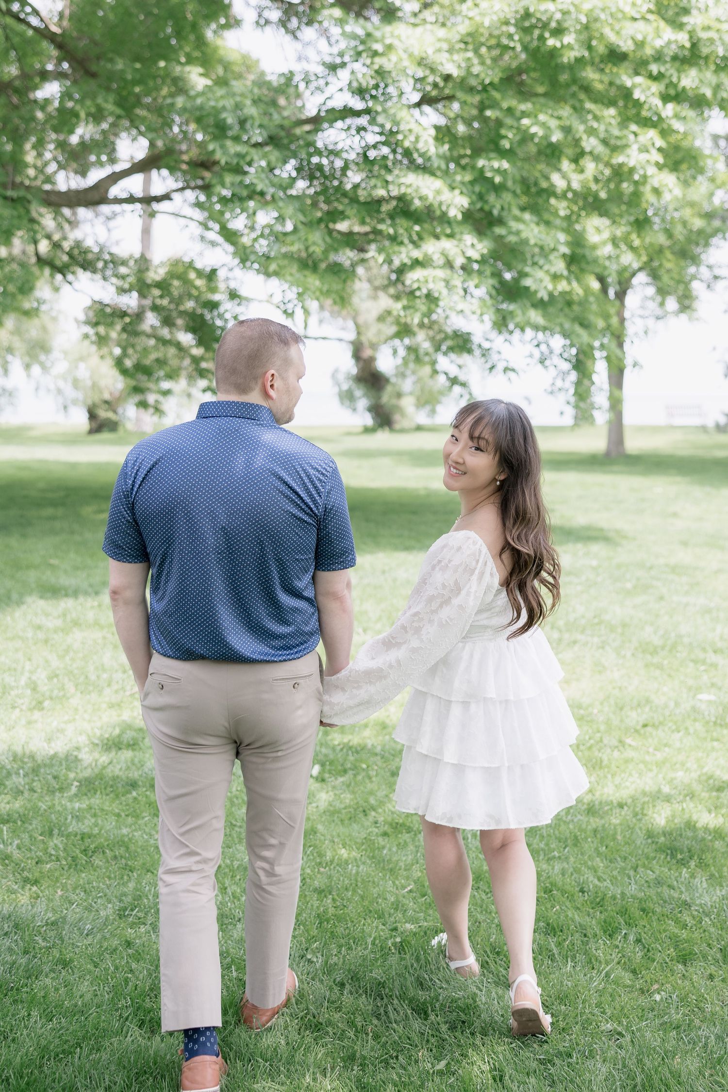 A couple walking together on green grass with trees in the background during a sunny day.
