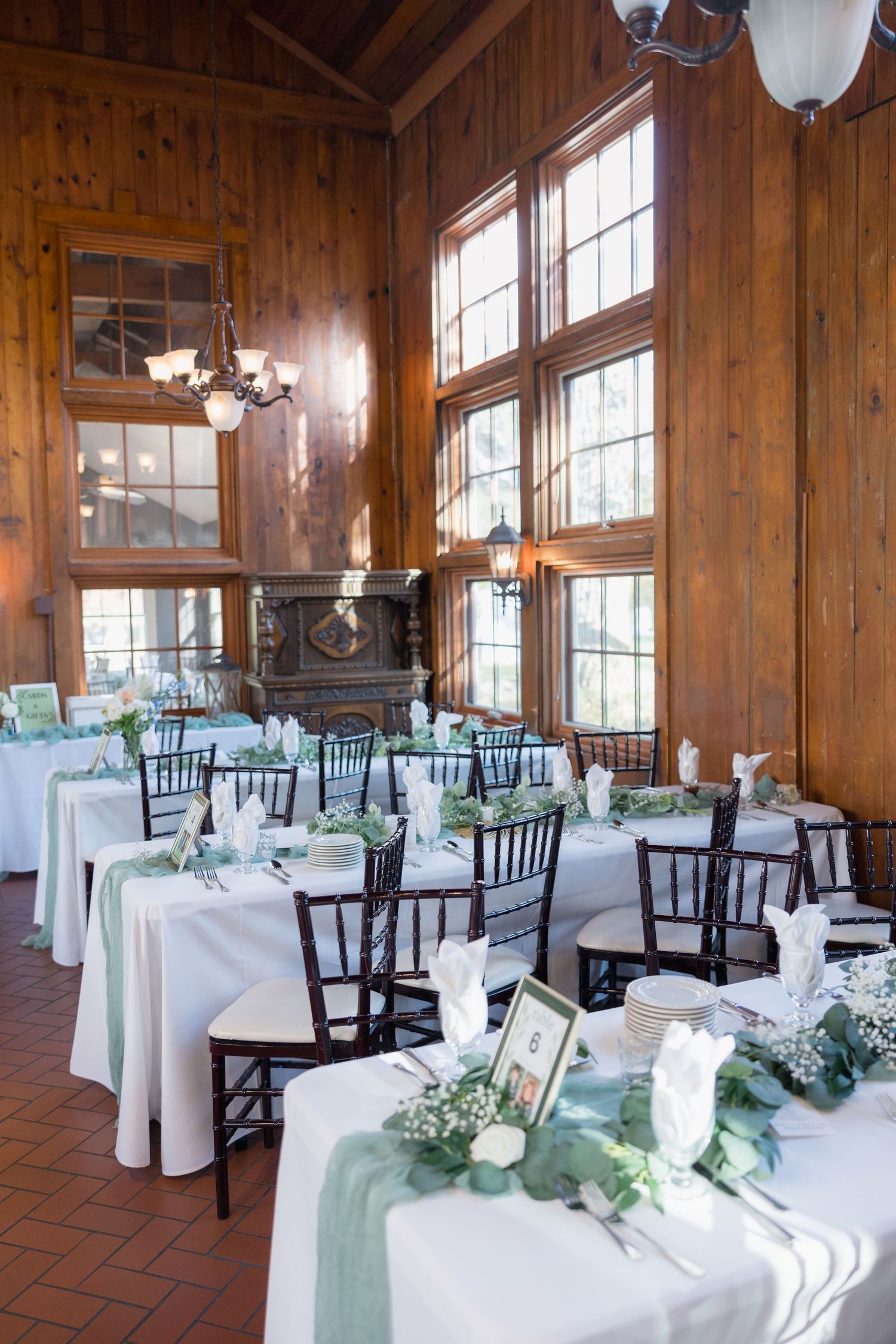 Rustic wooden reception hall with white tablecloths, black chairs, and sage green table runners.