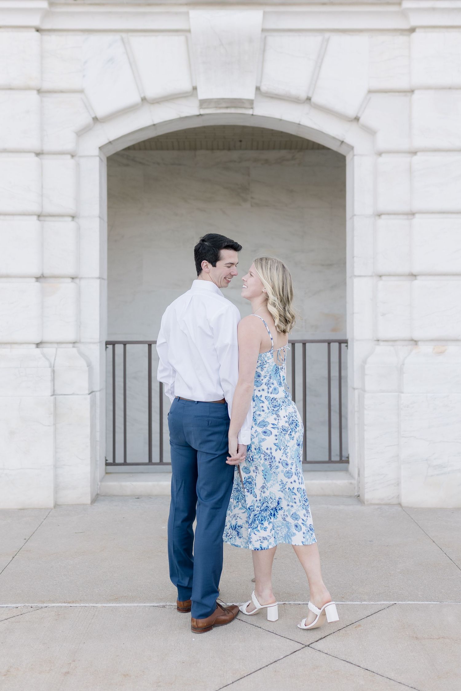 A couple shares an intimate moment while walking under arched stone architecture.