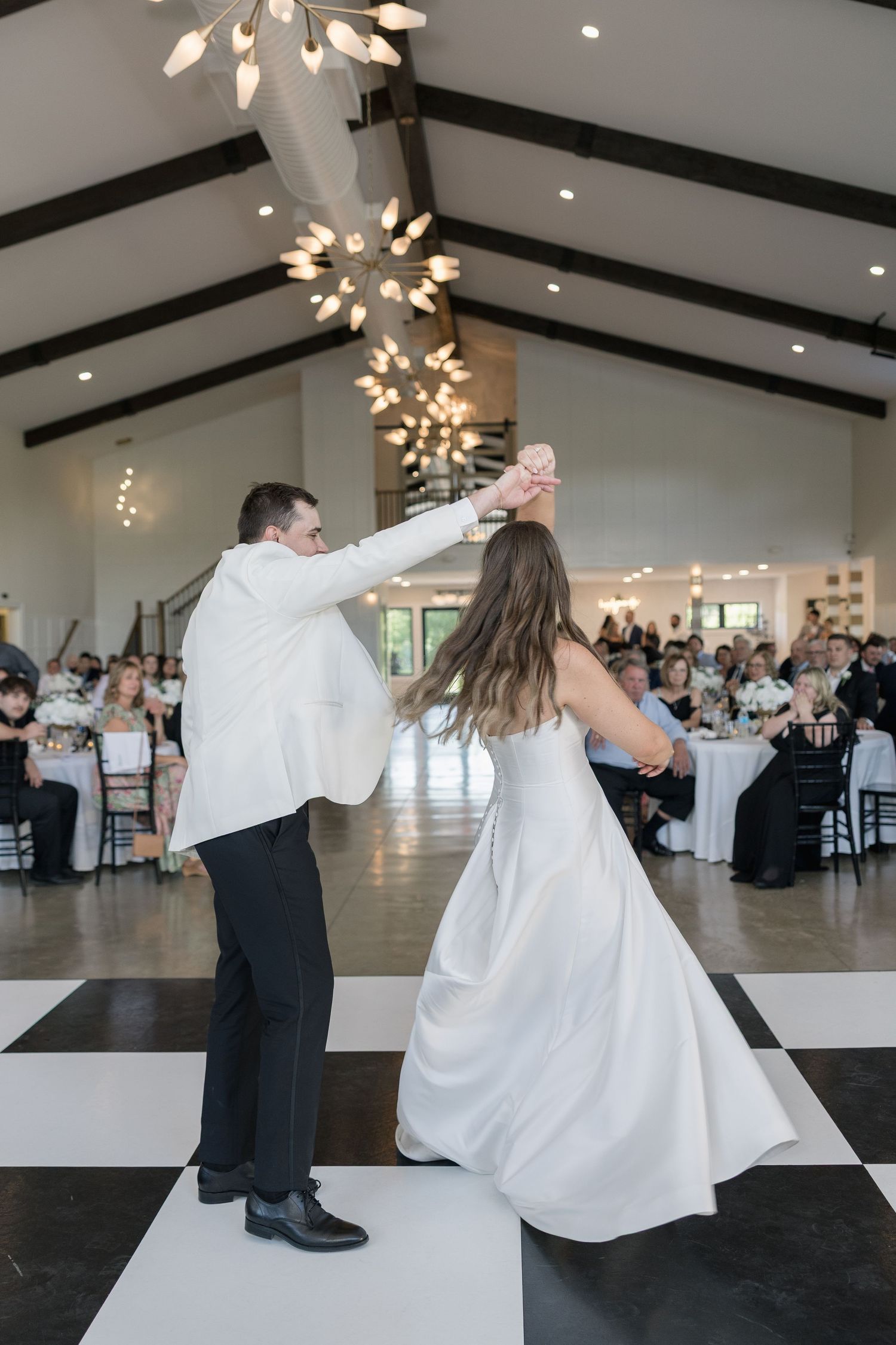 Bride and groom share first dance on checkered floor in a stunning wedding venue.