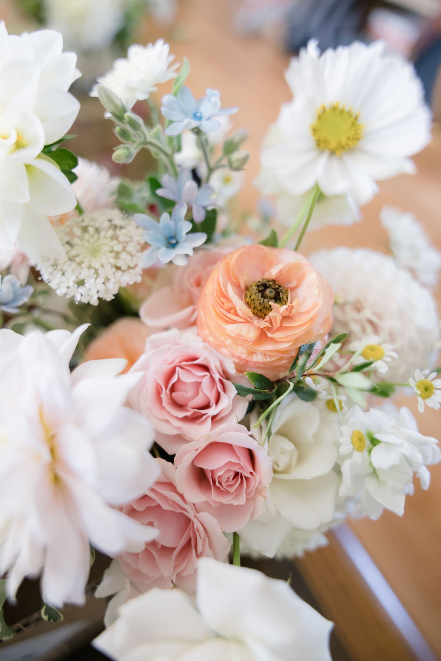 A delicate bouquet of pink roses, peach ranunculus, and white daisies with blue accents.