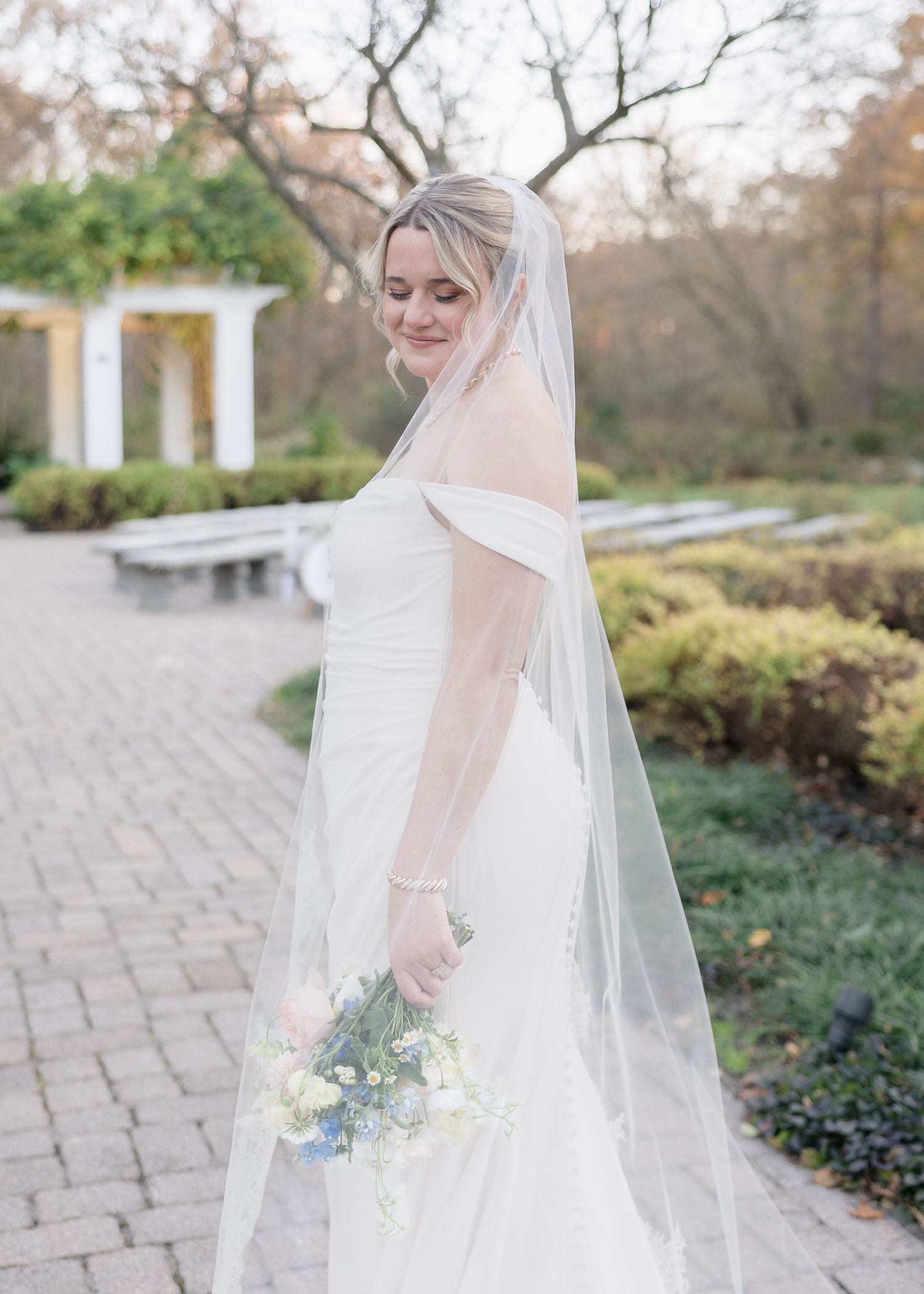 A bridal portrait showcasing an elegant white gown and long veil in a garden setting.