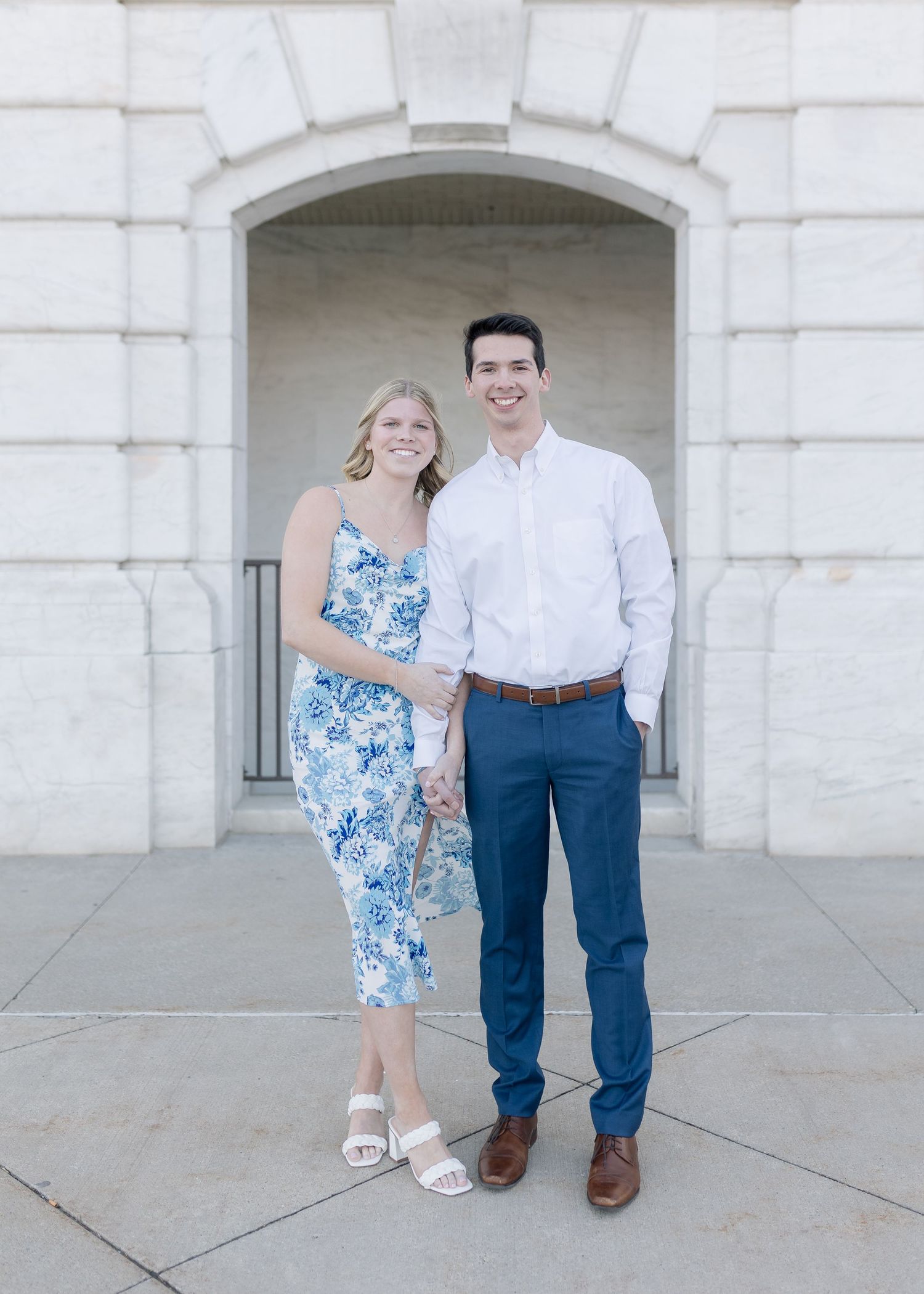 A couple stands together in front of a white stone archway, wearing a blue floral dress & button-down shirt. Detroit Michigan Art Institute.