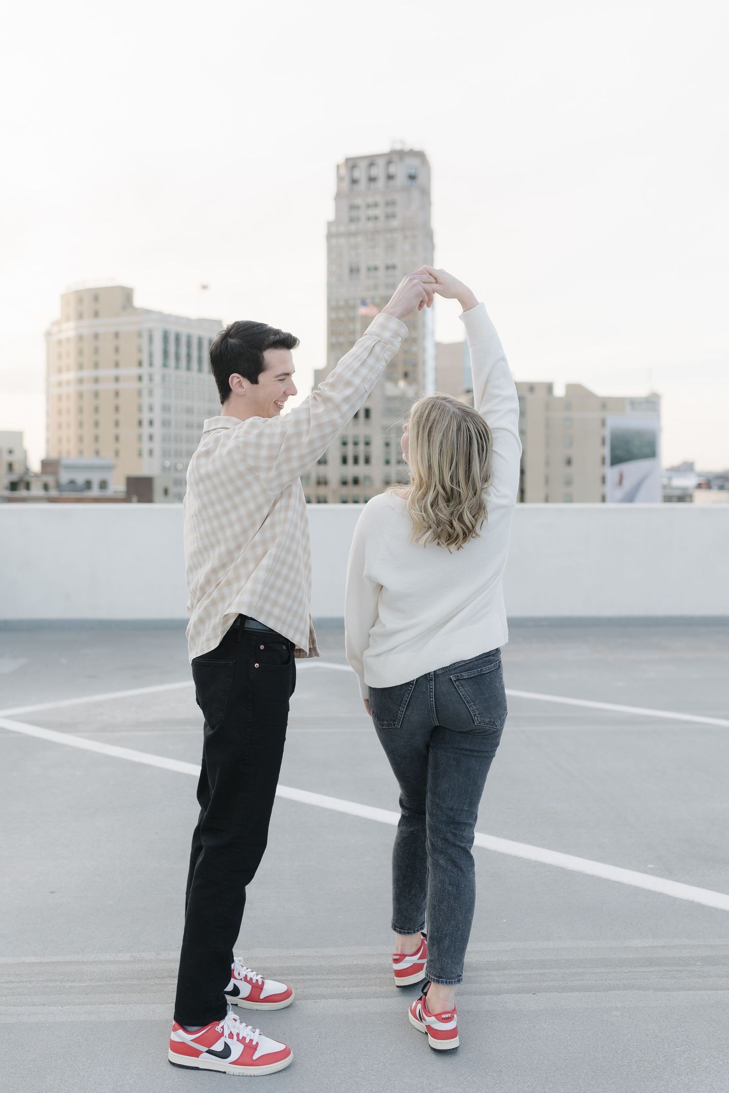 A couple dancing on an urban rooftop with city buildings in the background at dusk.