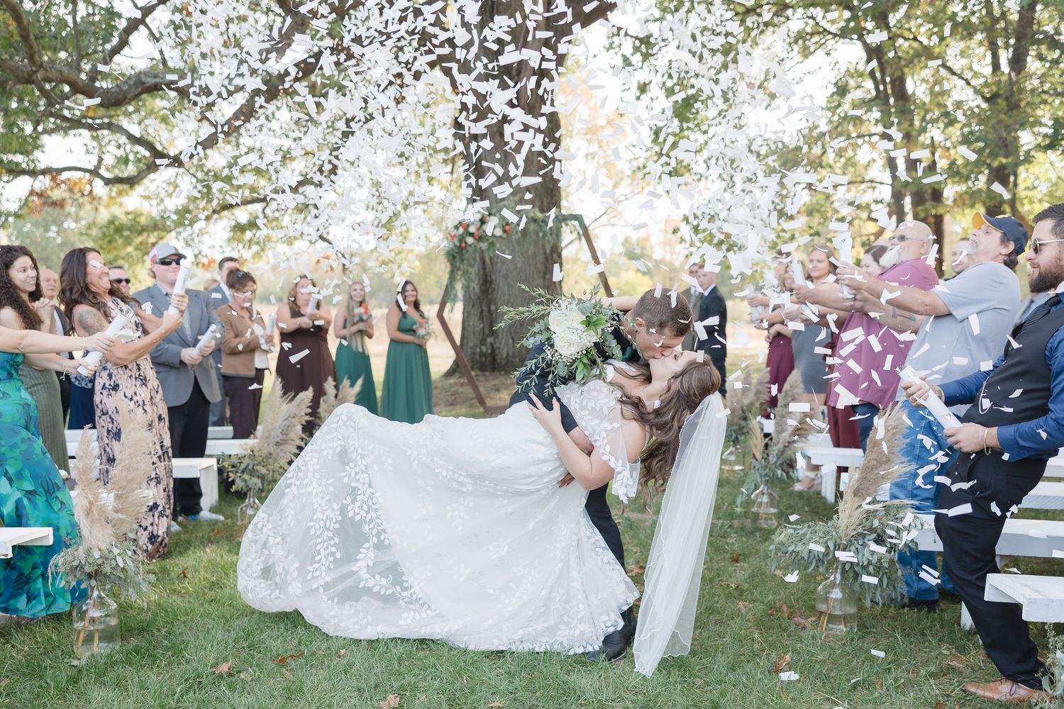Wedding celebration with guests seated outdoors under trees at sunset.