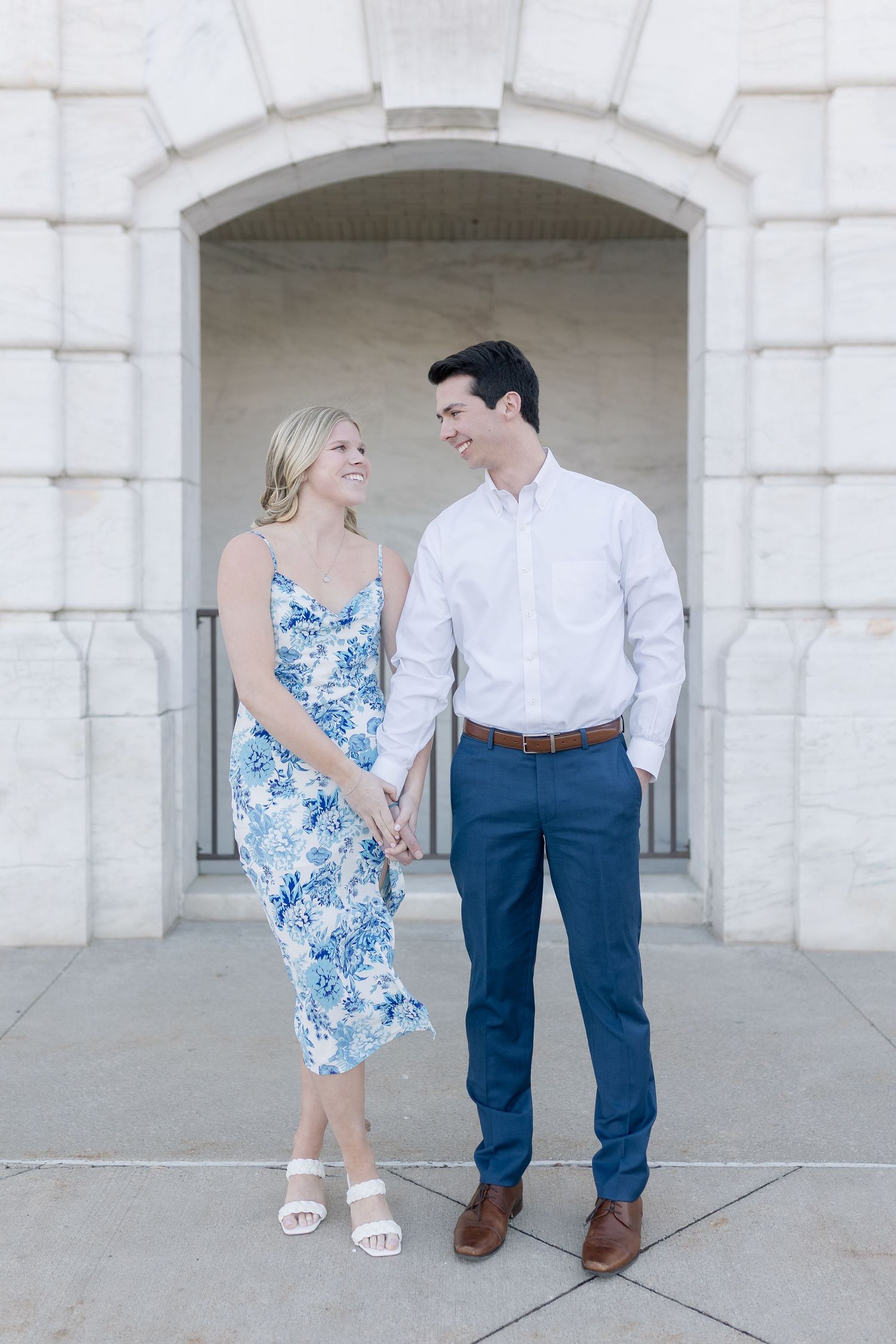 A couple in coordinated blue and white outfits stroll together against a white stone building backdrop.