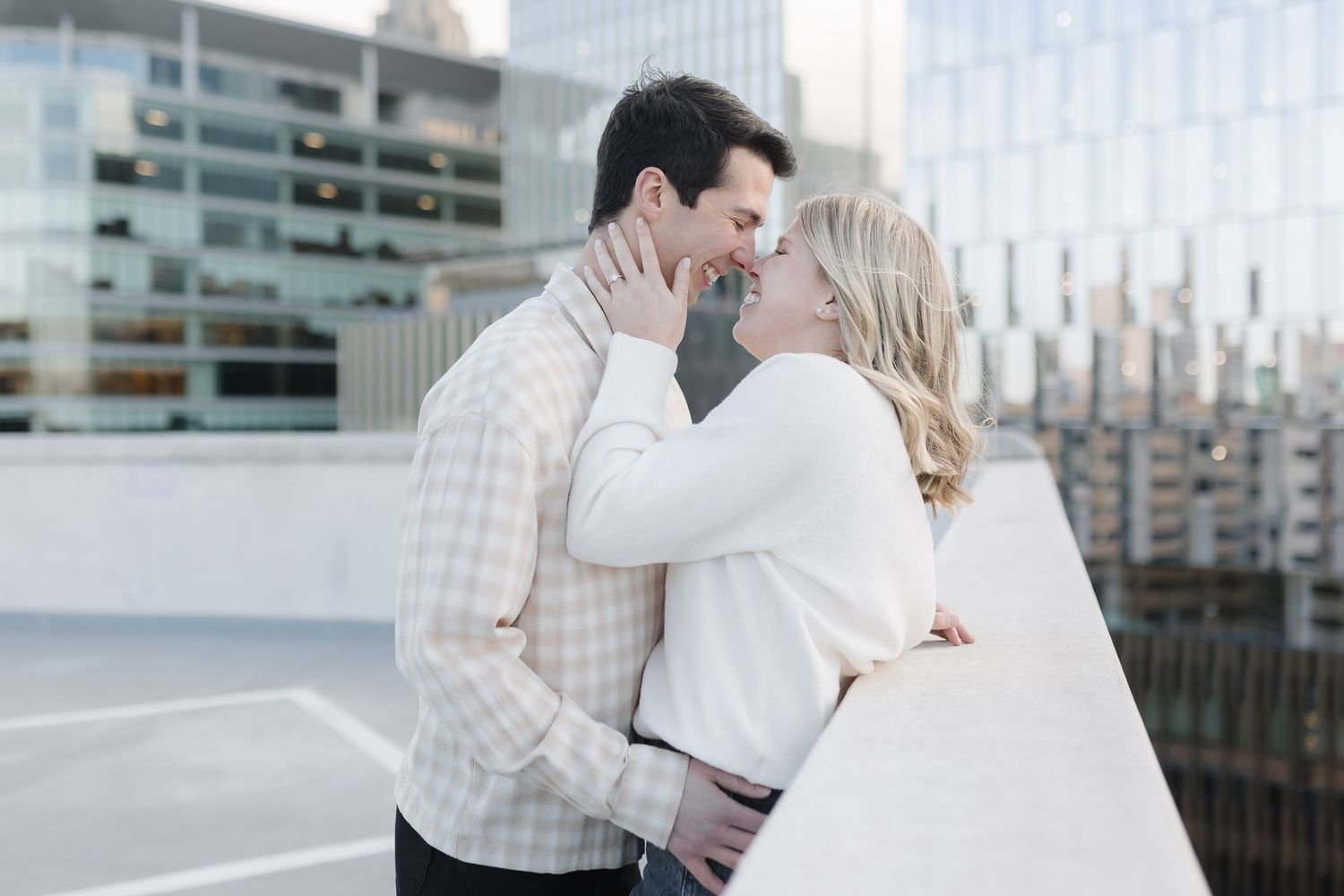 A romantic couple sharing an intimate moment on a rooftop parking deck with city buildings in the background.