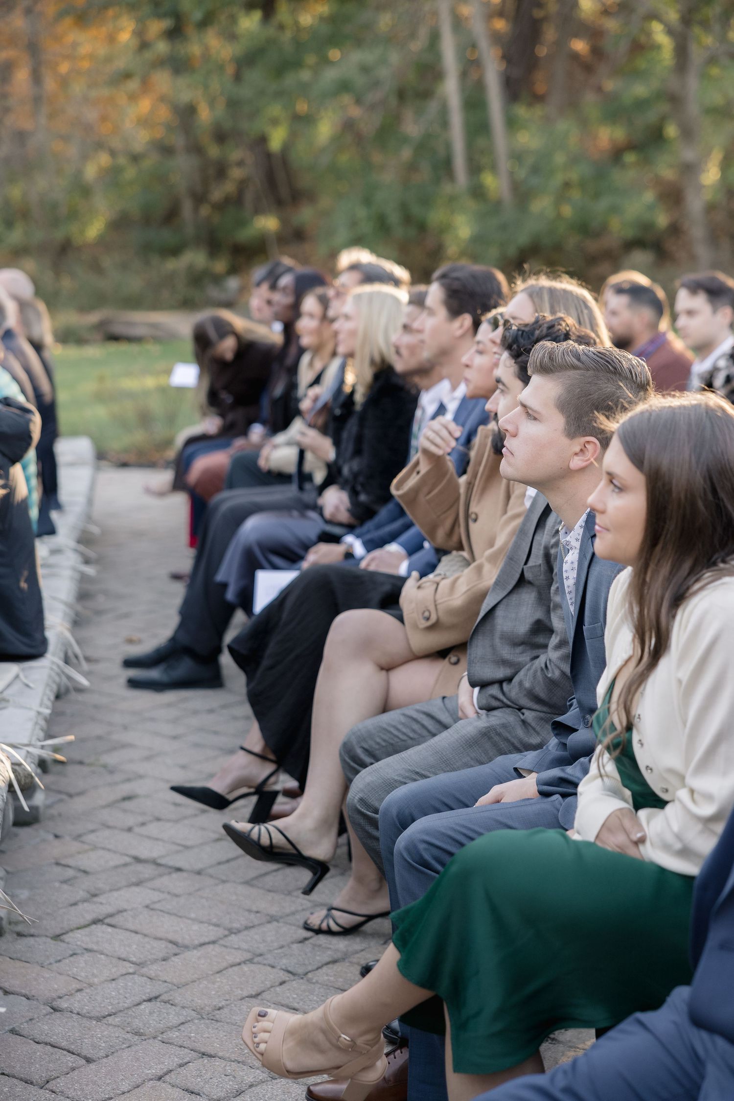 Wedding guests seated on rows of chairs watching an outdoor ceremony.
