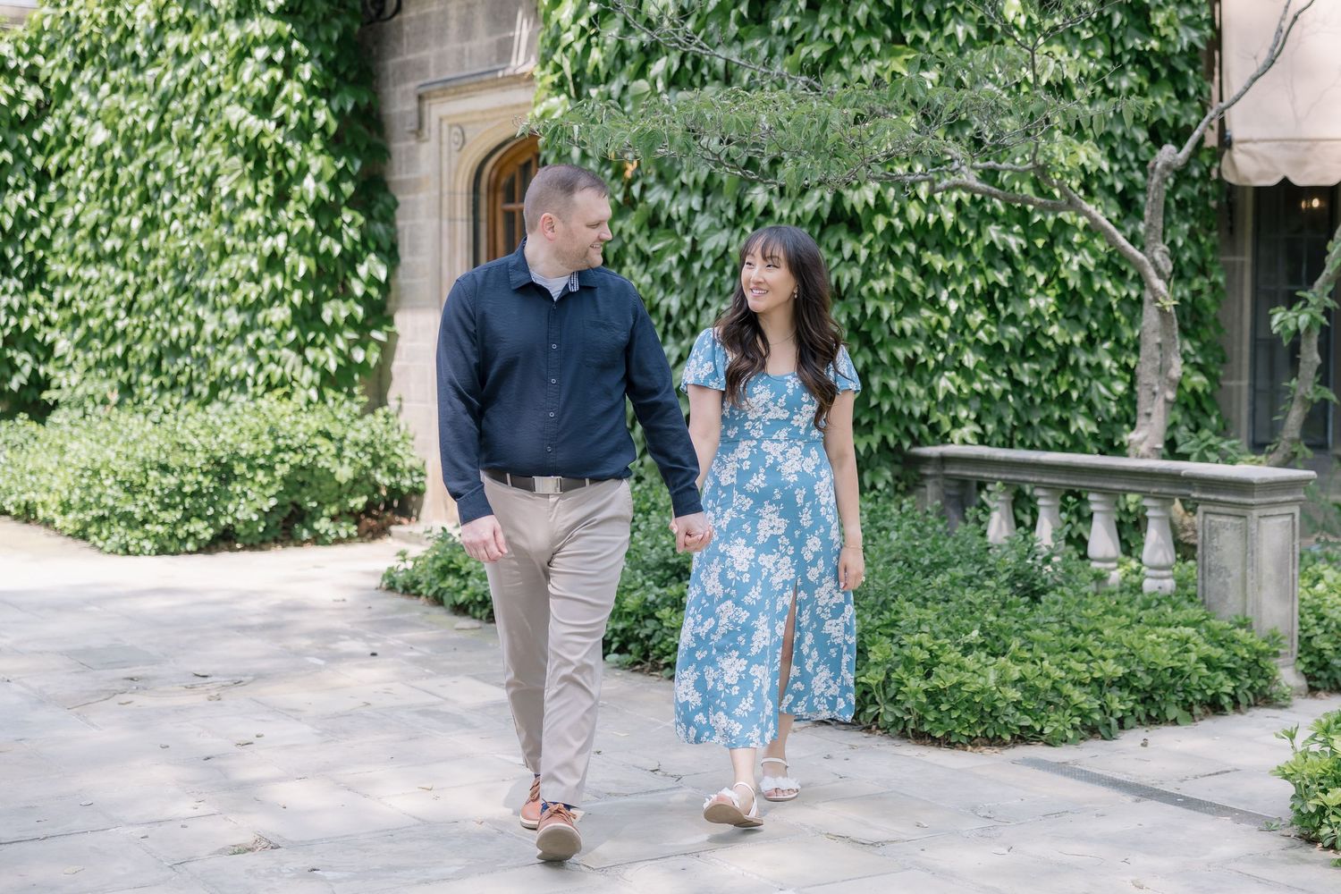 Couple walking together along ivy-covered wall during summer photoshoot.